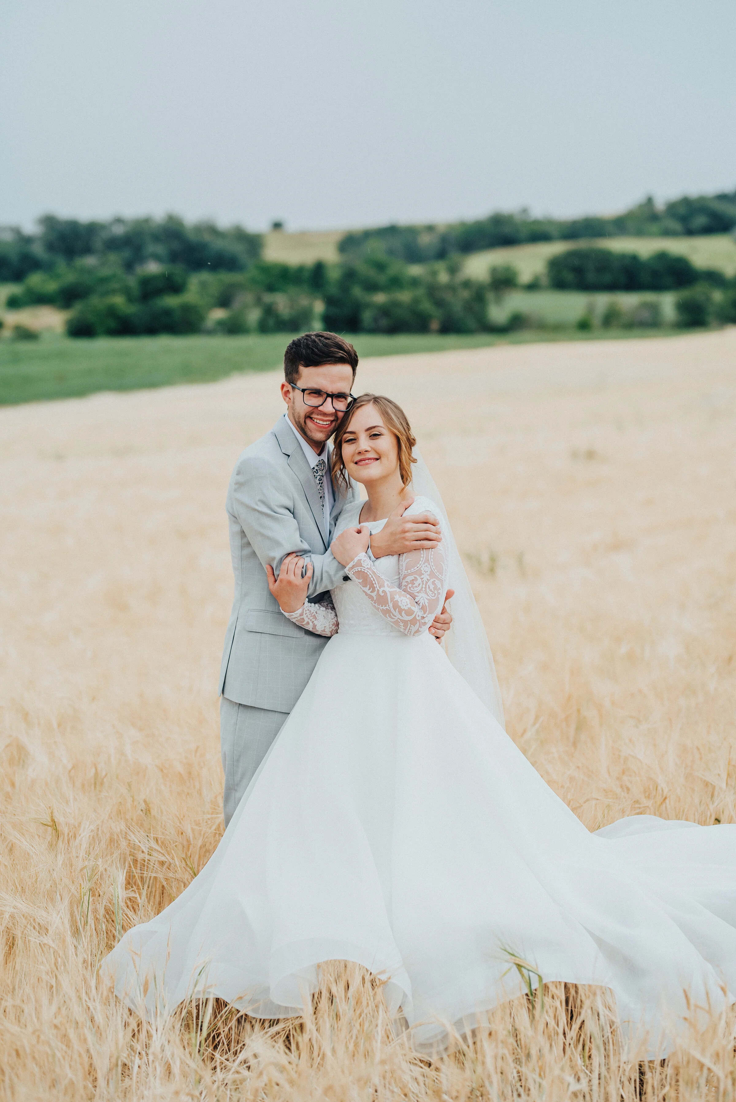  Kristi Alyse Photography captures first-look giddy grins during this Logan, Utah bridal session. bride and groom side hug, content bride and groom smiles, laced long sleeved ball gown wedding dress, long flowwy bridal train, black thick framed mens 