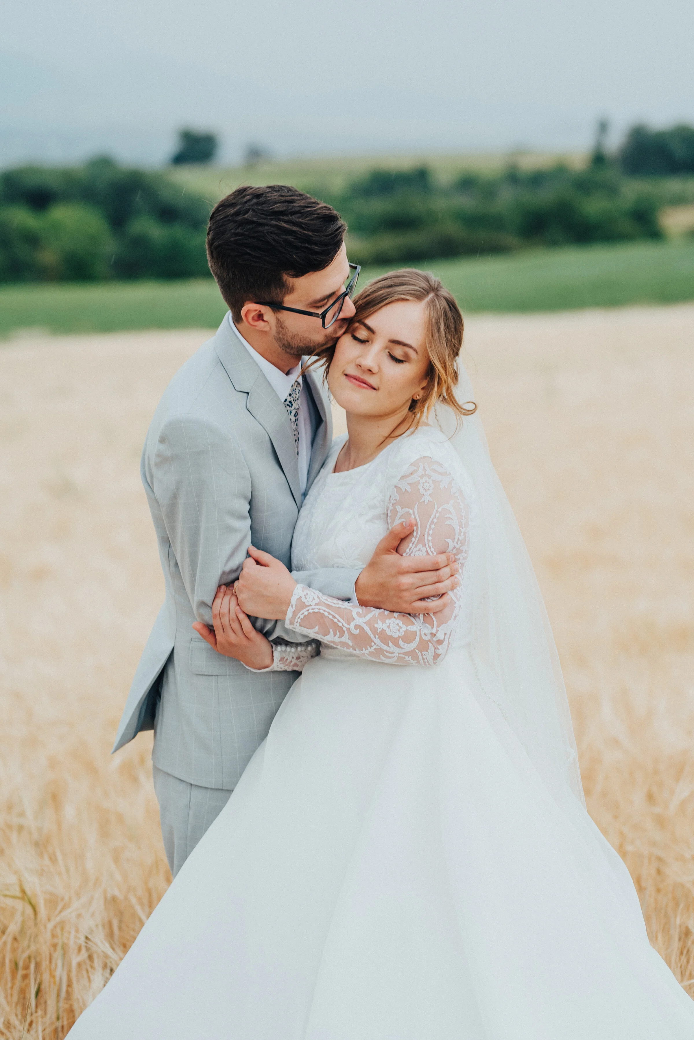 Kristi Alyse photography highlights this bride’s romantic ballgown wedding dress in this Logan, Utah bridal shoot. lace long sleeved wedding dress, ballgown long trained wedding dress, white plaid on a gray wedding suit, bride and groom hugging, gro…