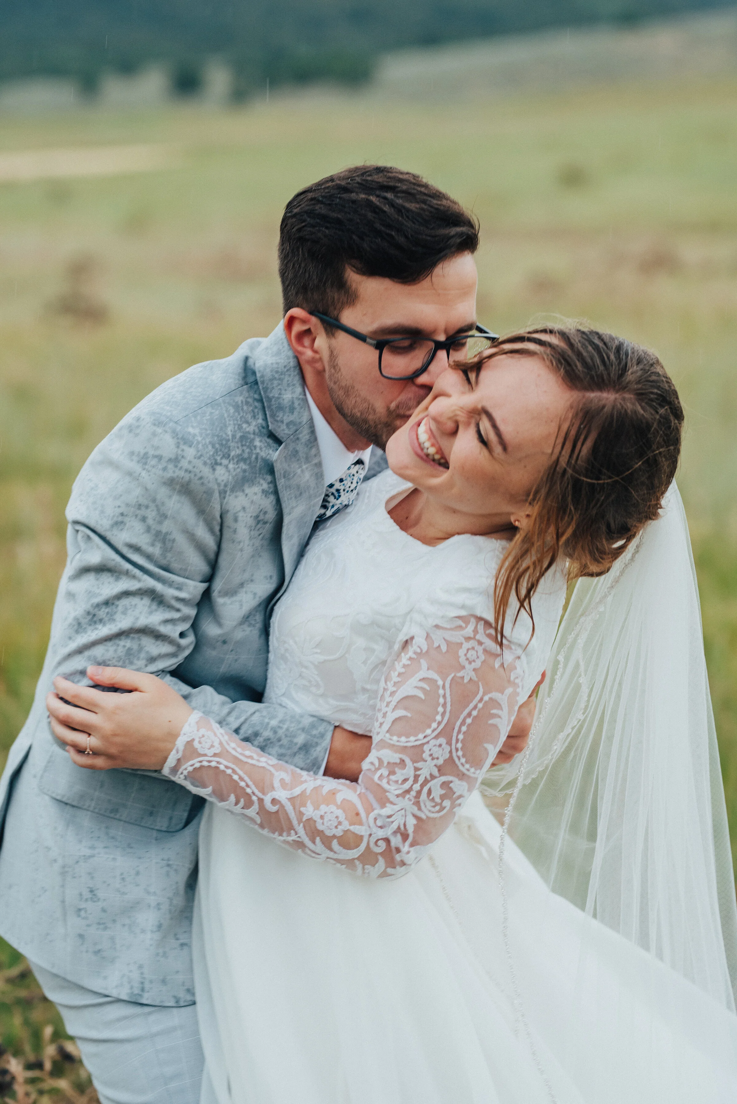  So much joy in one photo! This image from a rain-soaked bridal session by Kristi Alyse Photography was filled with fun, energy, and glee in Logan, Utah. bride and groom hugging in the rain, huge bridal grin, cheek kissing, playful bridal session, au