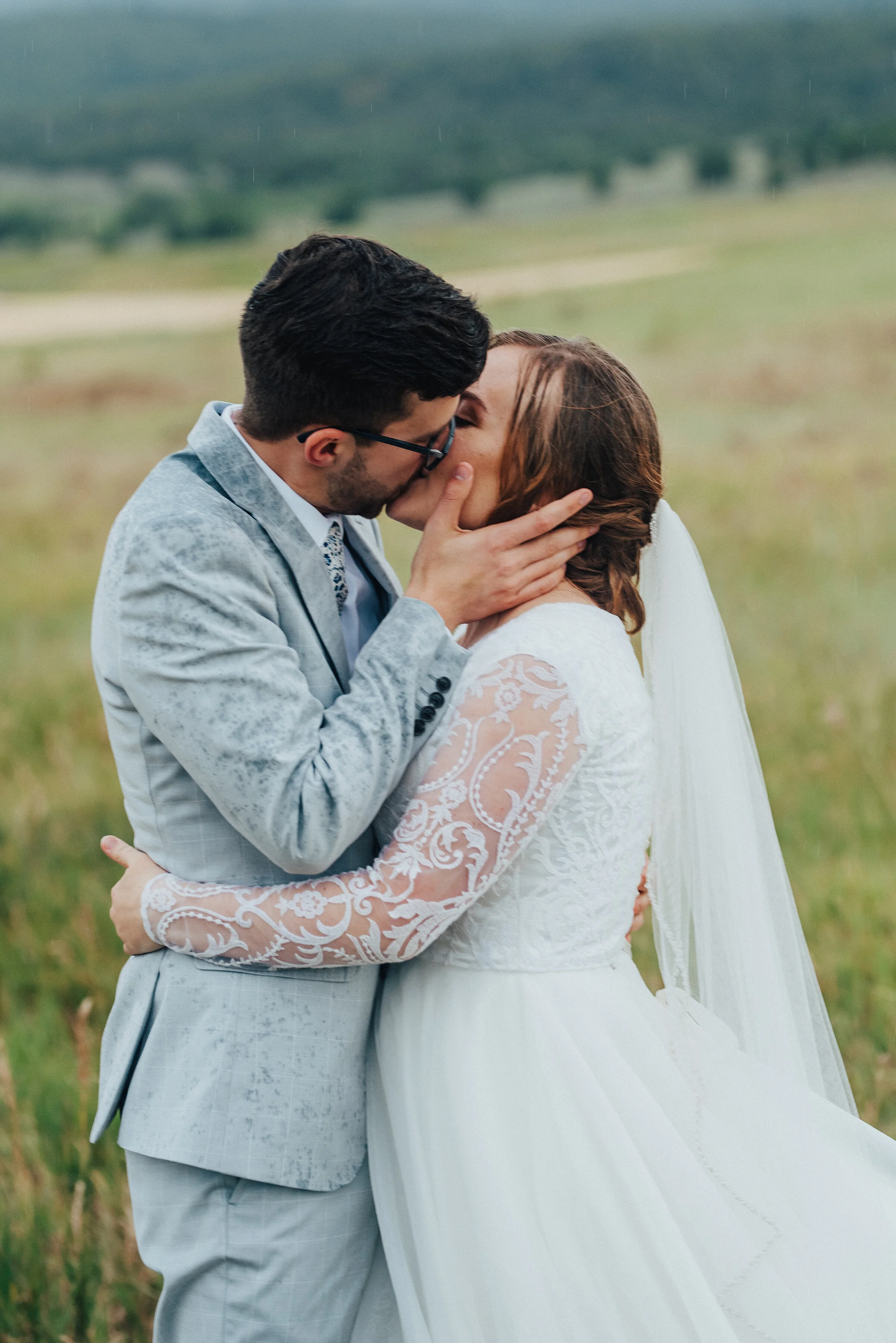 Emotional and rain soaked, this bridal session captured by Kristi Alyse Photography in Logan, Utah, was filled with passion and sneaky kisses. rainy bridal session, long beaded wedding veil, light gray plaid wedding suit, passionate bridal kissing, …
