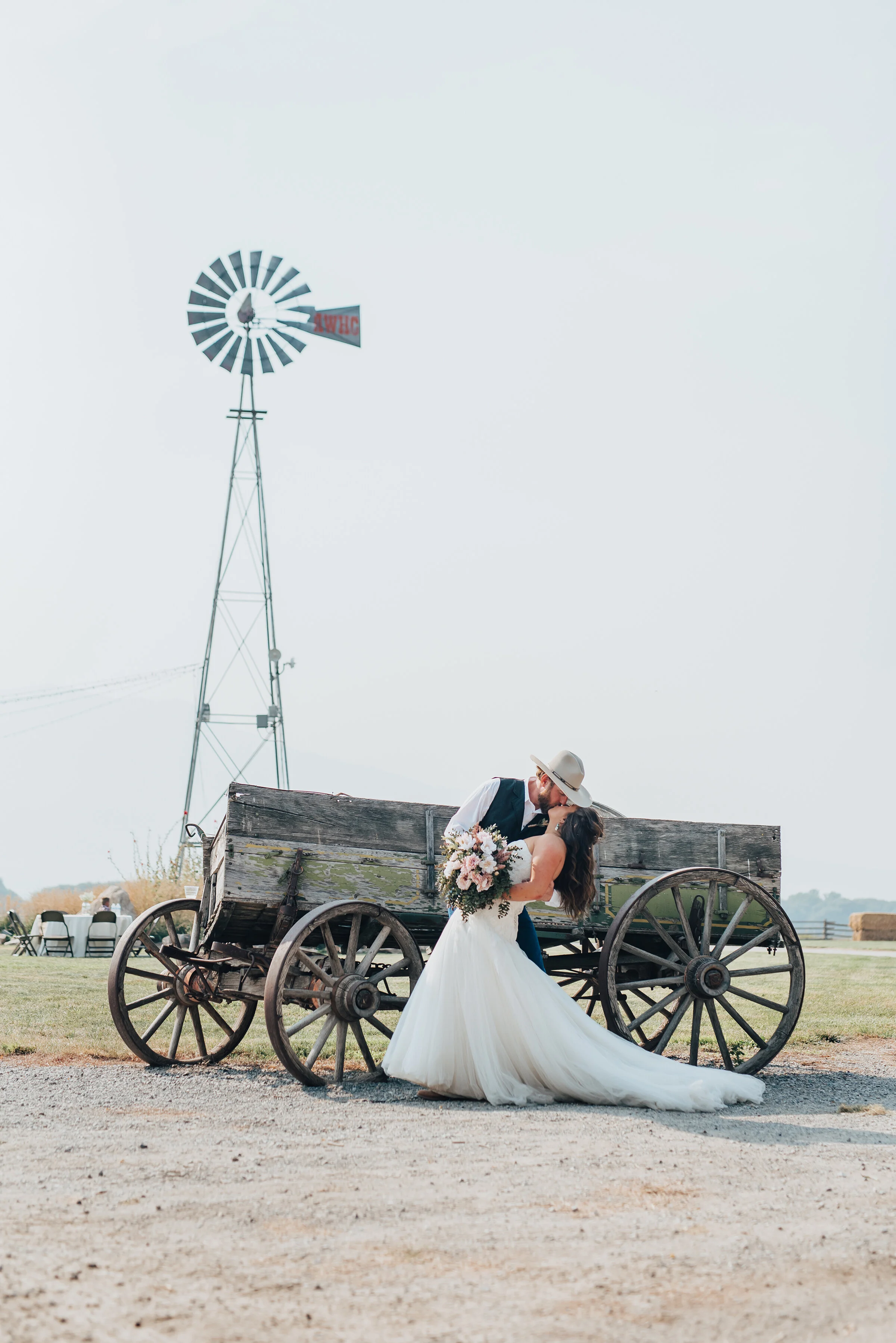  A traditional wooden wagon, rolling grass fields and windmill seal the perfect ambiance for this southern-styled outdoor wedding in Cache Valley, Utah, shot by Kristi Alyse Photography. lean back bride and groom kiss, white cowboy wedding hat, woode