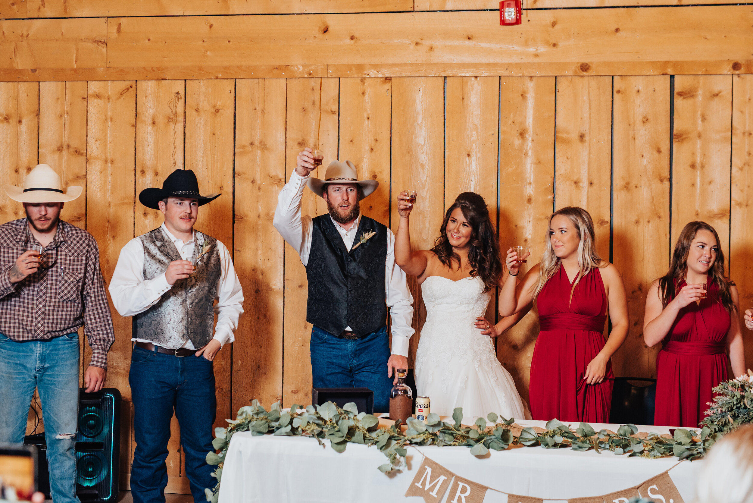  Kristi Alyse Photography captures a joyful toast at this southern-styled couple’s barn wedding in Welsville, Utah. barn wedding reception, eucalyptus wedding centerpiece garland, wedding party, ruby red bridesmaids dresses, groomsmen wrangler jeans,