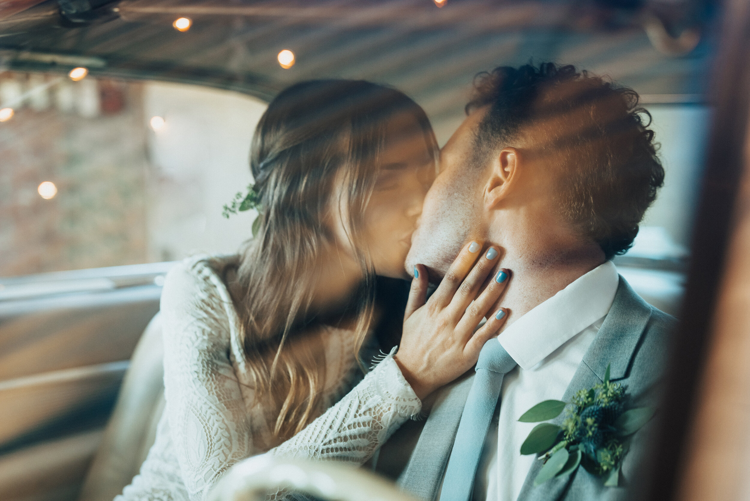 On their way to be married in Provo, Utah, Kristi Alyse Photography captures the bride stealing kisses from her groom in their car. ombre blue gel nails, bohemian long sleeved lace wedding dress, blue gray wedding suit, succulent wedding boutonniere…