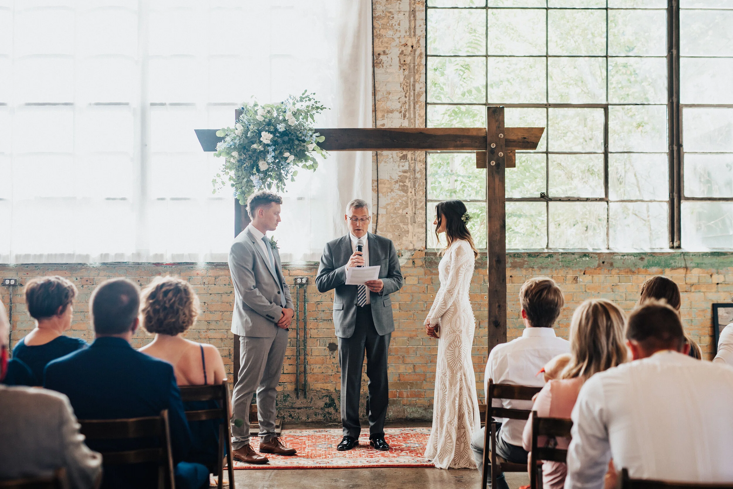  Large industrial windows and a floral adorned  wedding arch provide the perfect serene setting as Kristi Alyse Photography captures bride and groom exchange vows at their wedding ceremony in Provo, Utah. Bright Building Provo Utah, wedding vows, boh