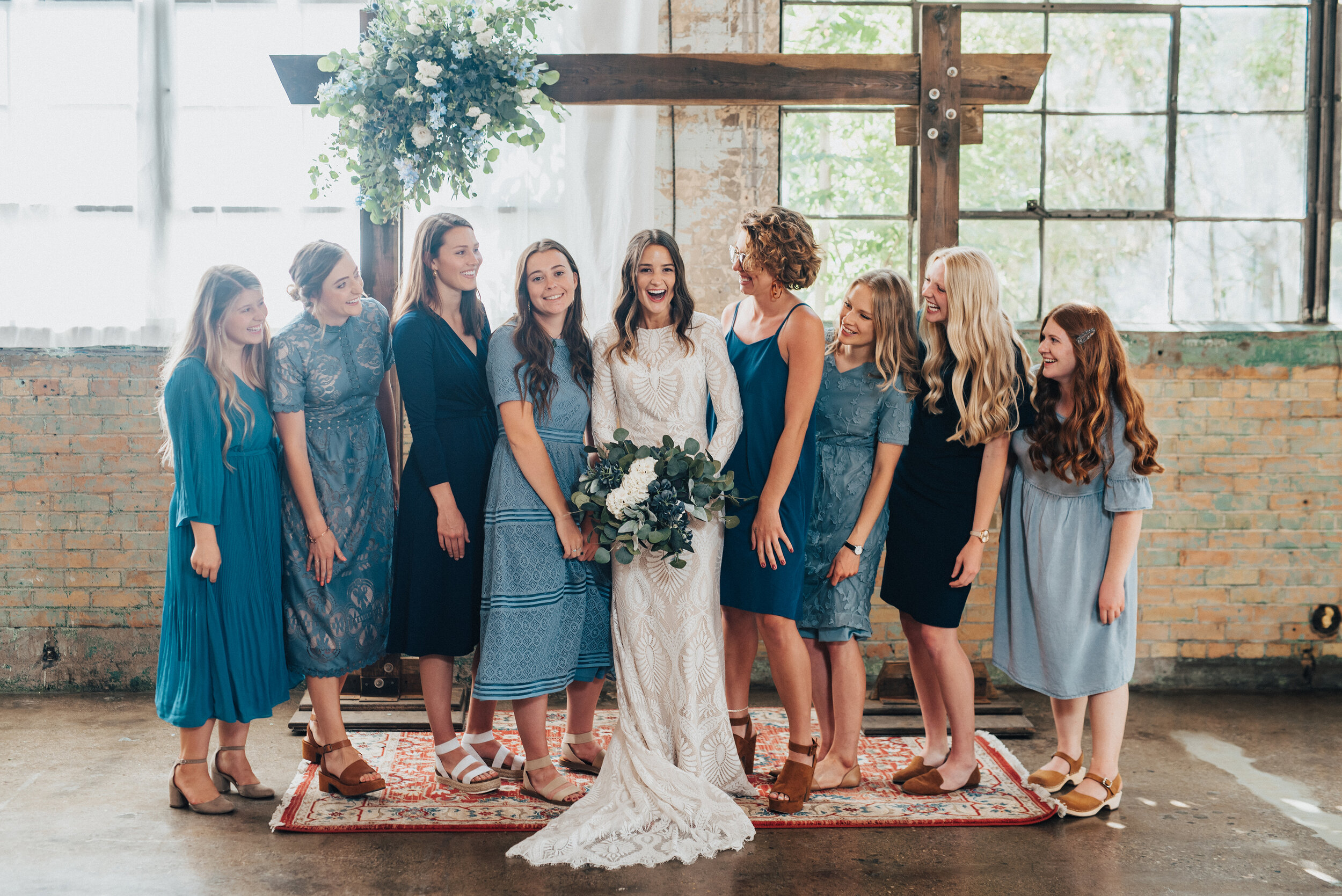 Kristi Alyse Photography captured candid smiles as bridesmaids in gray-blue dresses surround this bohemian bride at the Bright Building in Provo, Utah. blue medium length bridesmaids dresses, modest blue bridesmaids dresses, bohemian blue bridesmaid…