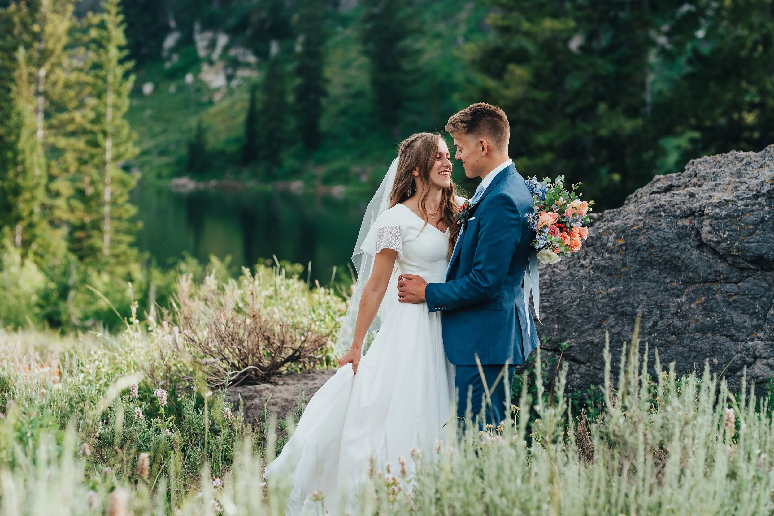 Stunning bride in a modest white wedding dress with her wildflower bridal bouquet in an almost-kiss position with her groom at tony grove for their mountain formals. Mountain wedding photography wildflower bridal bouquet modest wedding dress with ve…