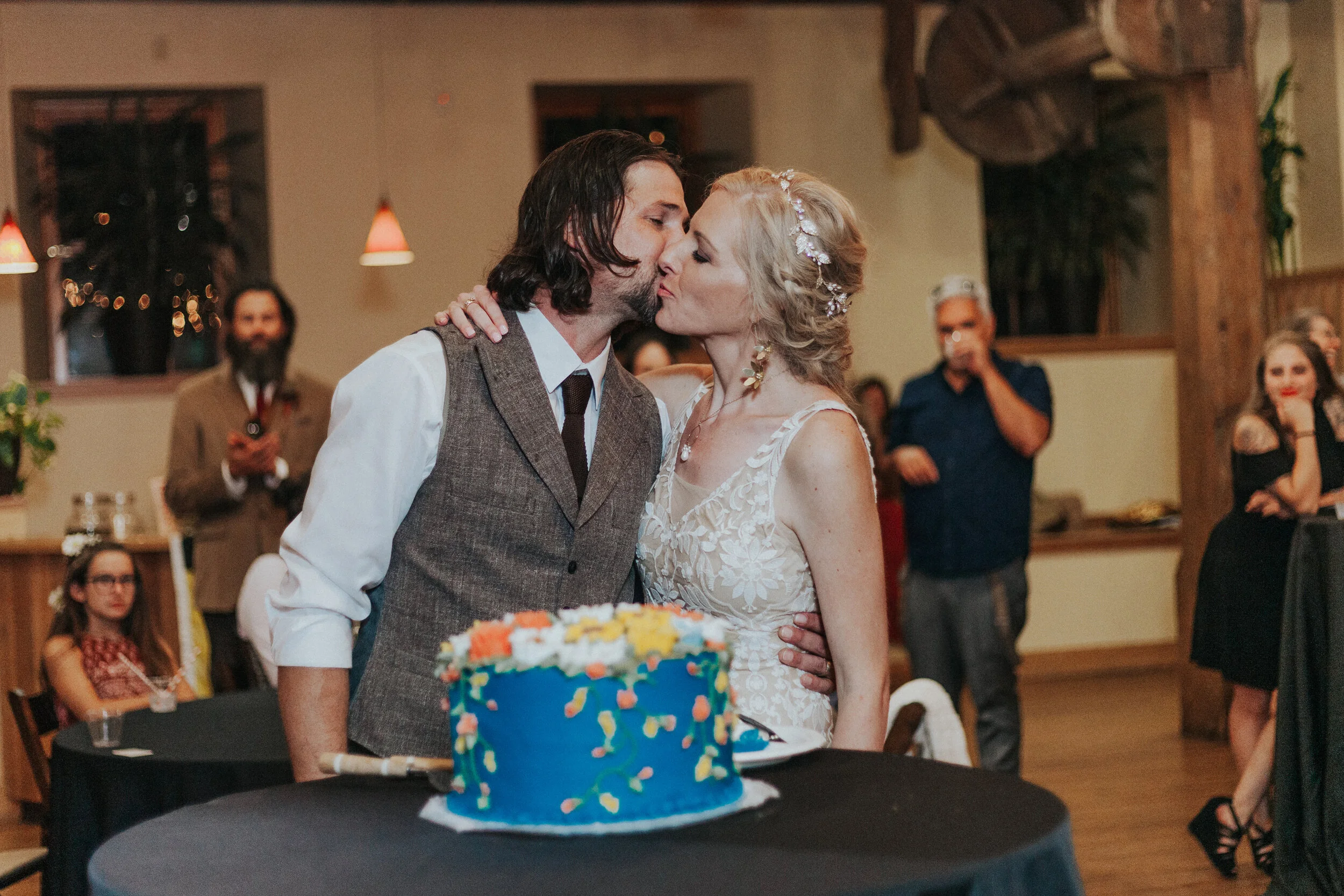  Bride and groom cutting the cake at their boho wedding that is blue with white and orange flowers on it by Kristi Alyse Photography in Nothern Utah. boho chic wedding ideas how to plan a boho wedding cake ceremony during wedding planning your weddin
