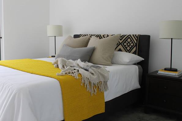 A tribal pattern rug is draped over an upholstered headboard for a custom look. Bright yellow and white serve as freshening elements.
