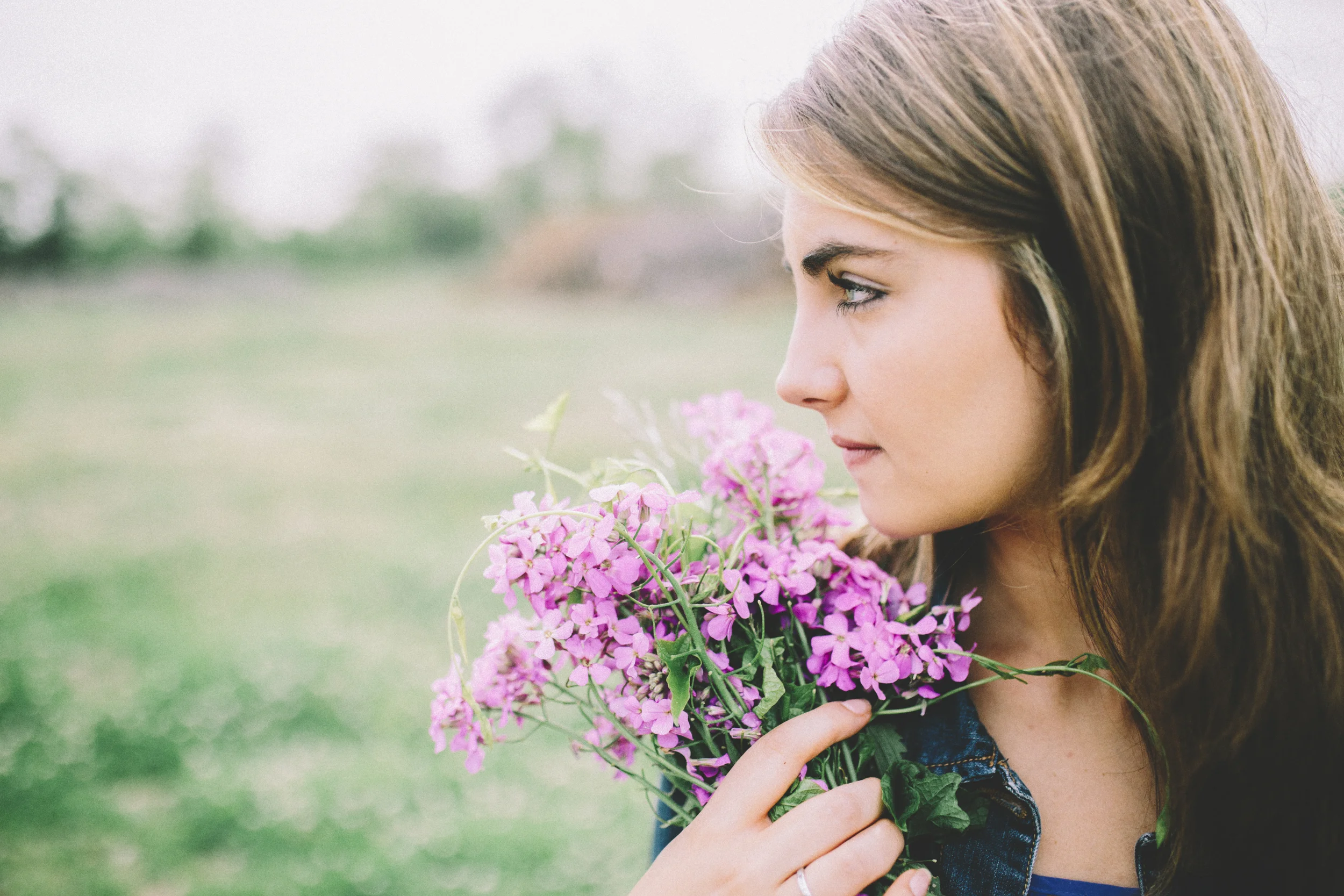 A woman with brown hair holding pink flowers outdoors on a cloudy day.