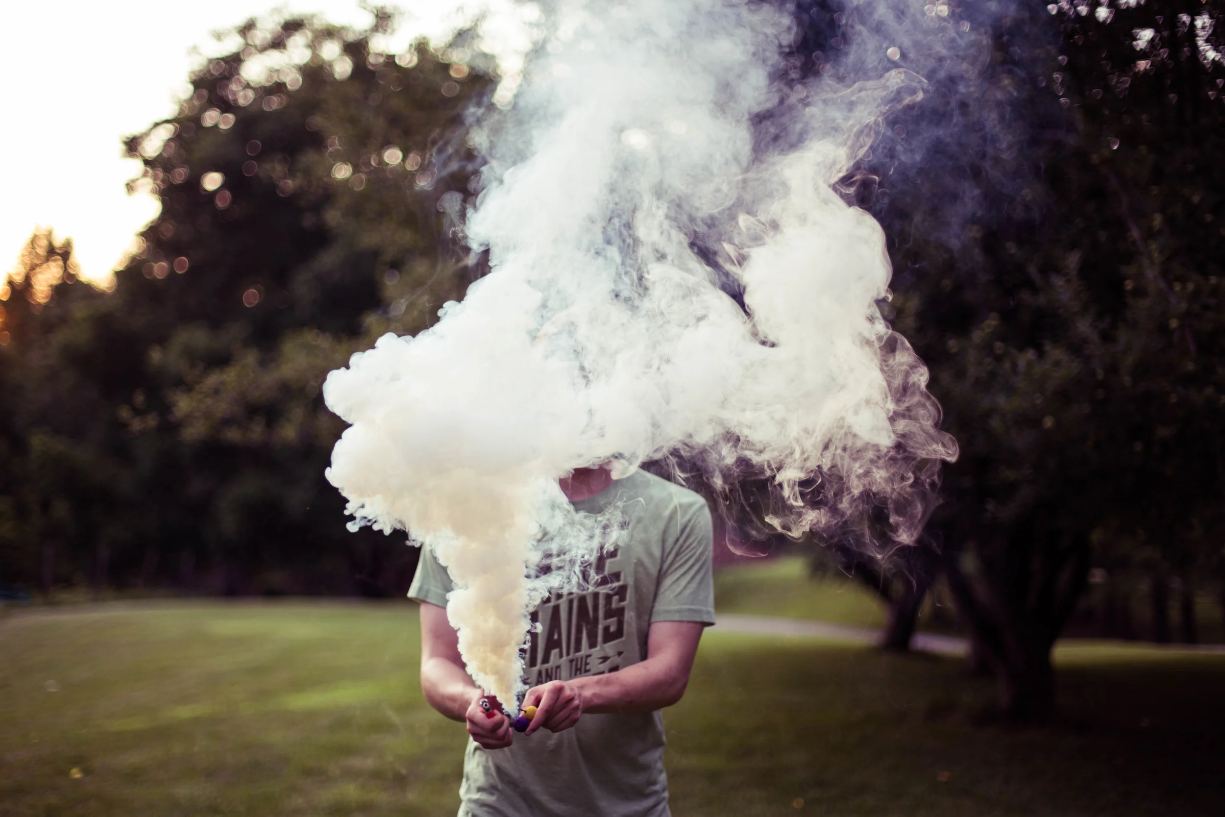 A person standing outdoors with smoke or vapor obscuring their face, holding a smoking device.