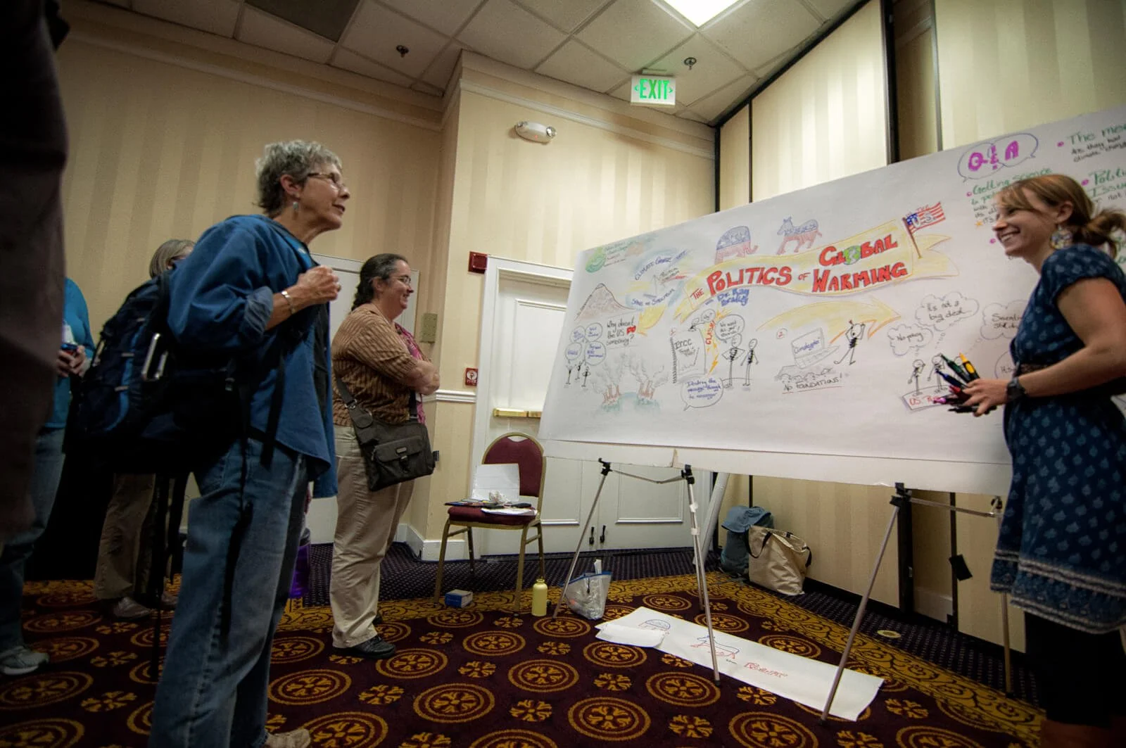 people standing in ballroom looking at hand drawn visual notes and talking with woman graphic recorder