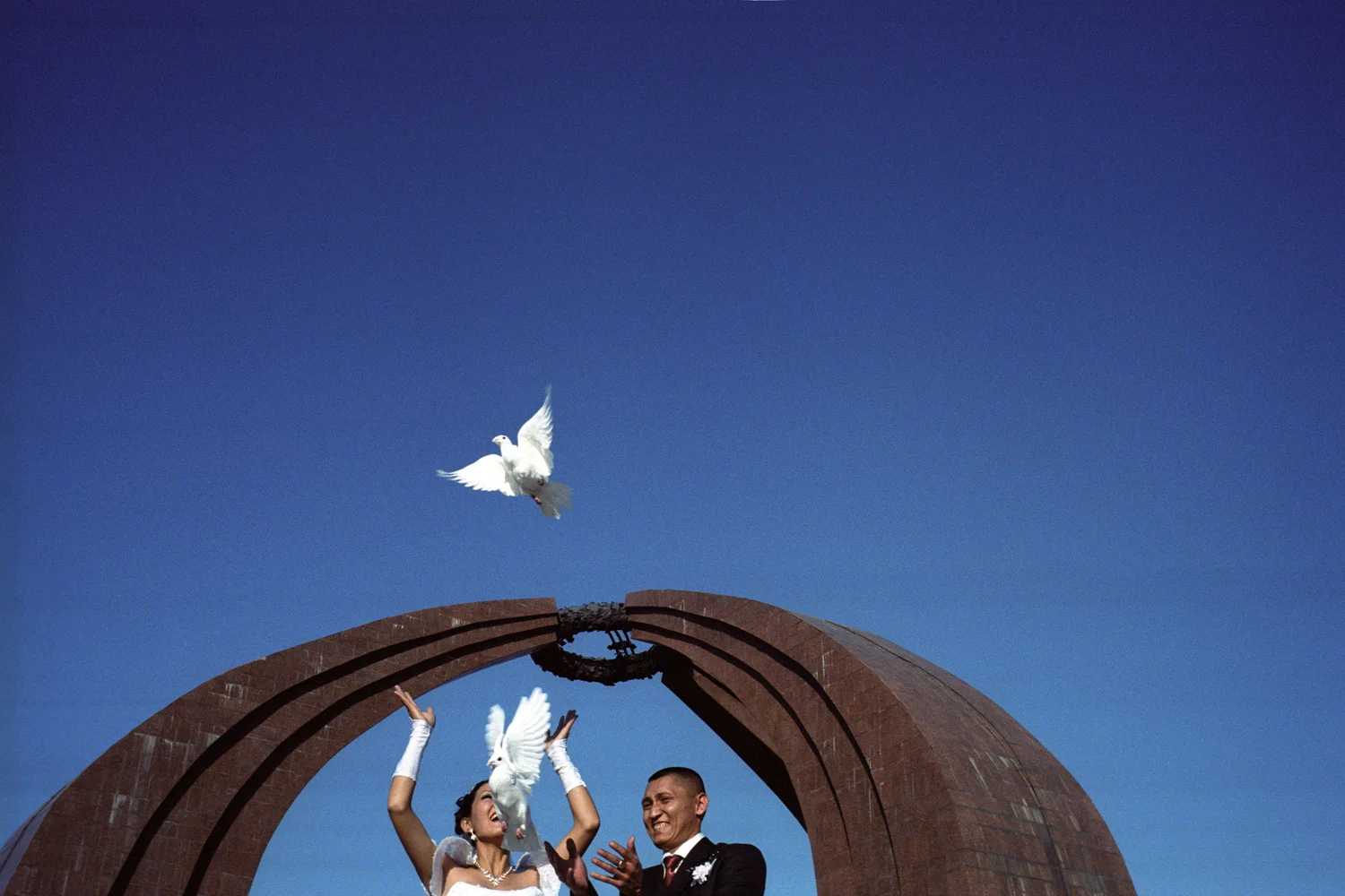 Newlyweds who have not been married through kidnapping pose for photographs on Victory Square. The custom of releasing doves comes from Russia. Kyrgyz marriage rituals mix Russian and Western influences with their own nomadic and shamanistic practises. Bishkek, Kyrgyzstan.