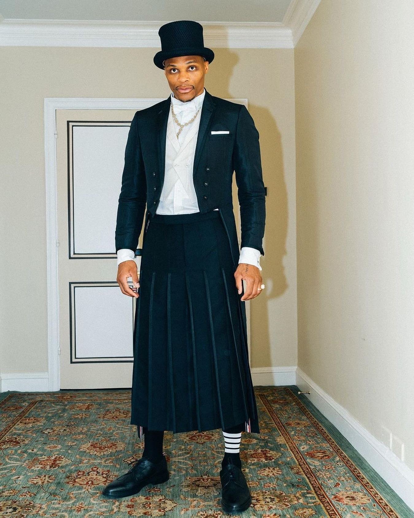 Russell Westbrook wears an elongated ankle length tailcoat in black silk moiré with tipping, white tie vest in white silk moiré, ankle length pleated skirt in 3-ply mohair and wing collar shirt.