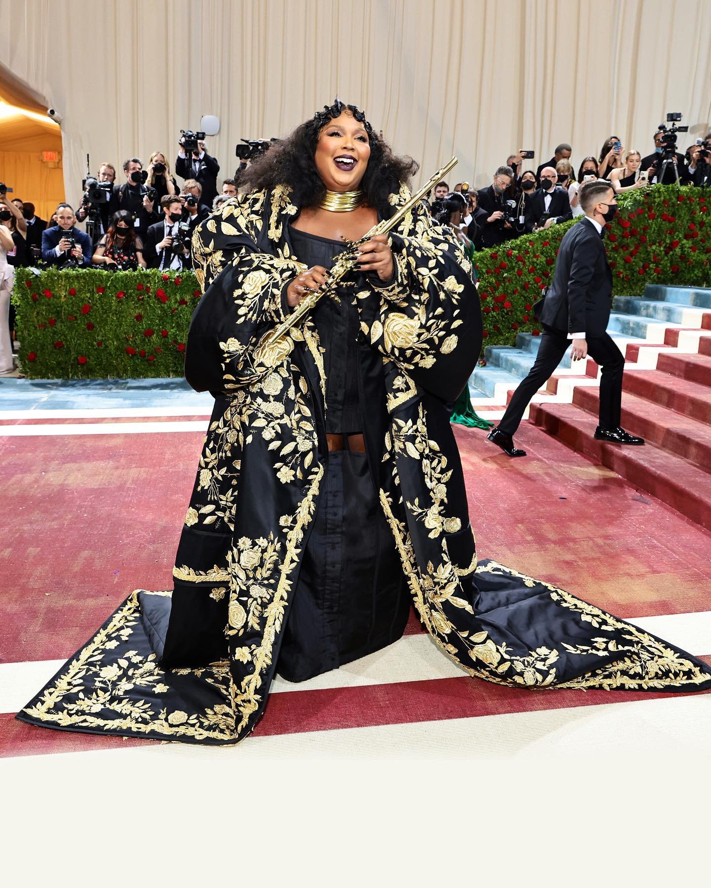 Lizzo wears a black silk moiré exaggerated hip corset dress, dropped skirt with an oversized chesterfield black duchess satin coat with gold rose, foliage bullion and silk satin stitch embroidery. 
