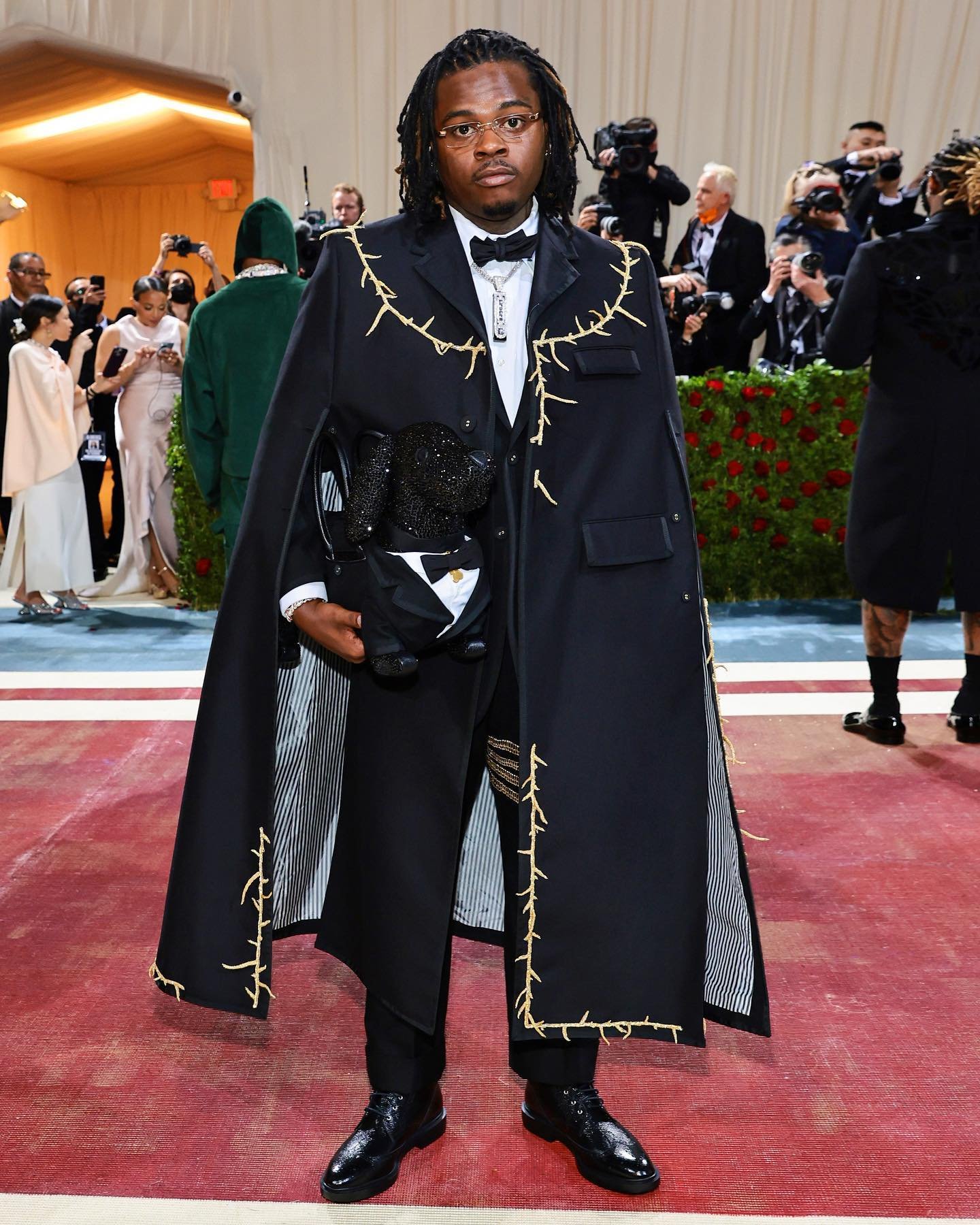Gunna wears a long cape in 3-ply mohair with gold bullion and beaded thorns embroidery over a suit in 3-ply mohair with gold 4-bar embroidery.
