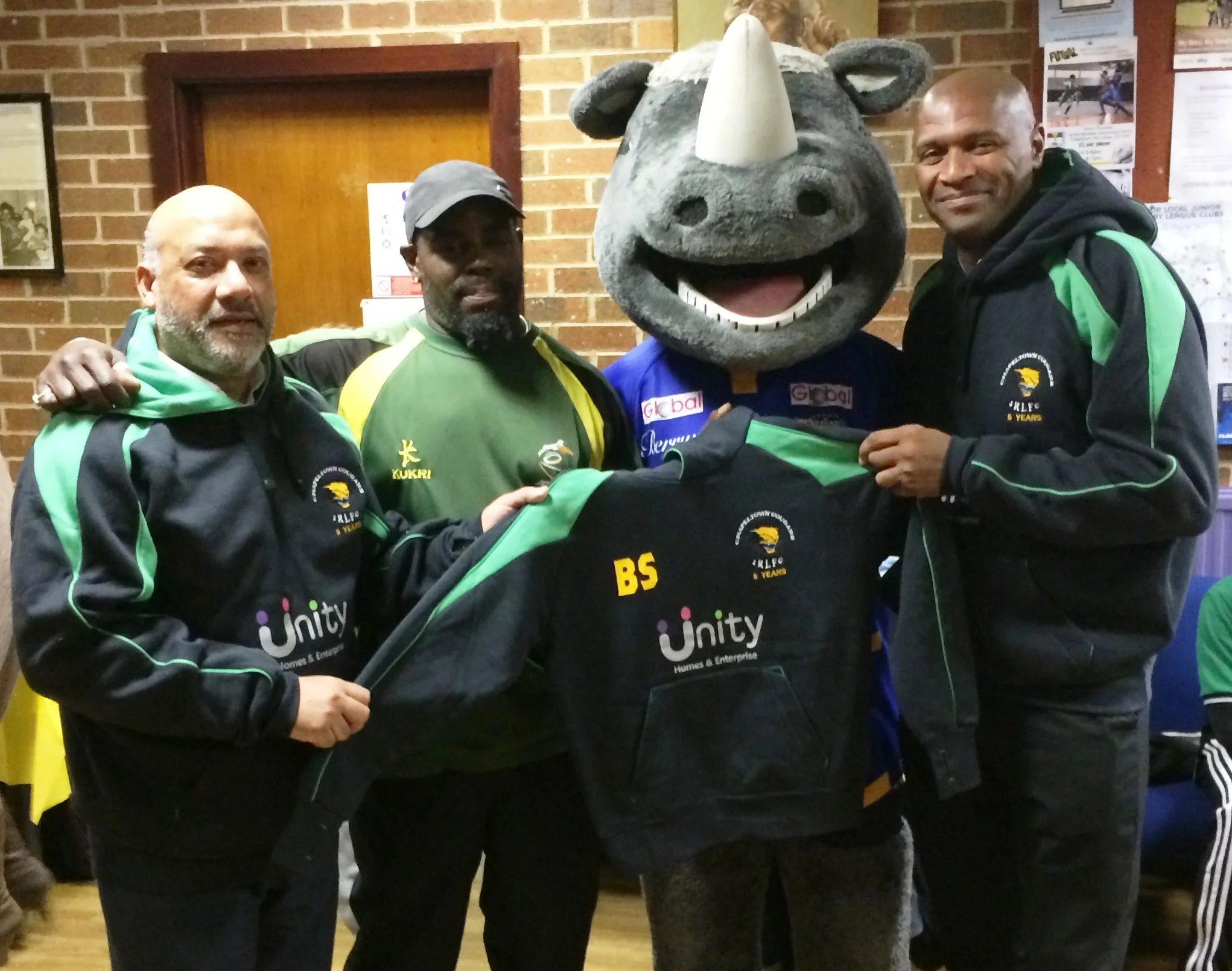 Unity Homes and Enterprise chief executive Ali Akbor (left) and director of regeneration Wayne Noteman (right) present Chapeltown Cougars head coach Steve Walker with a new hoodie, watched by Ronnie the Rhino