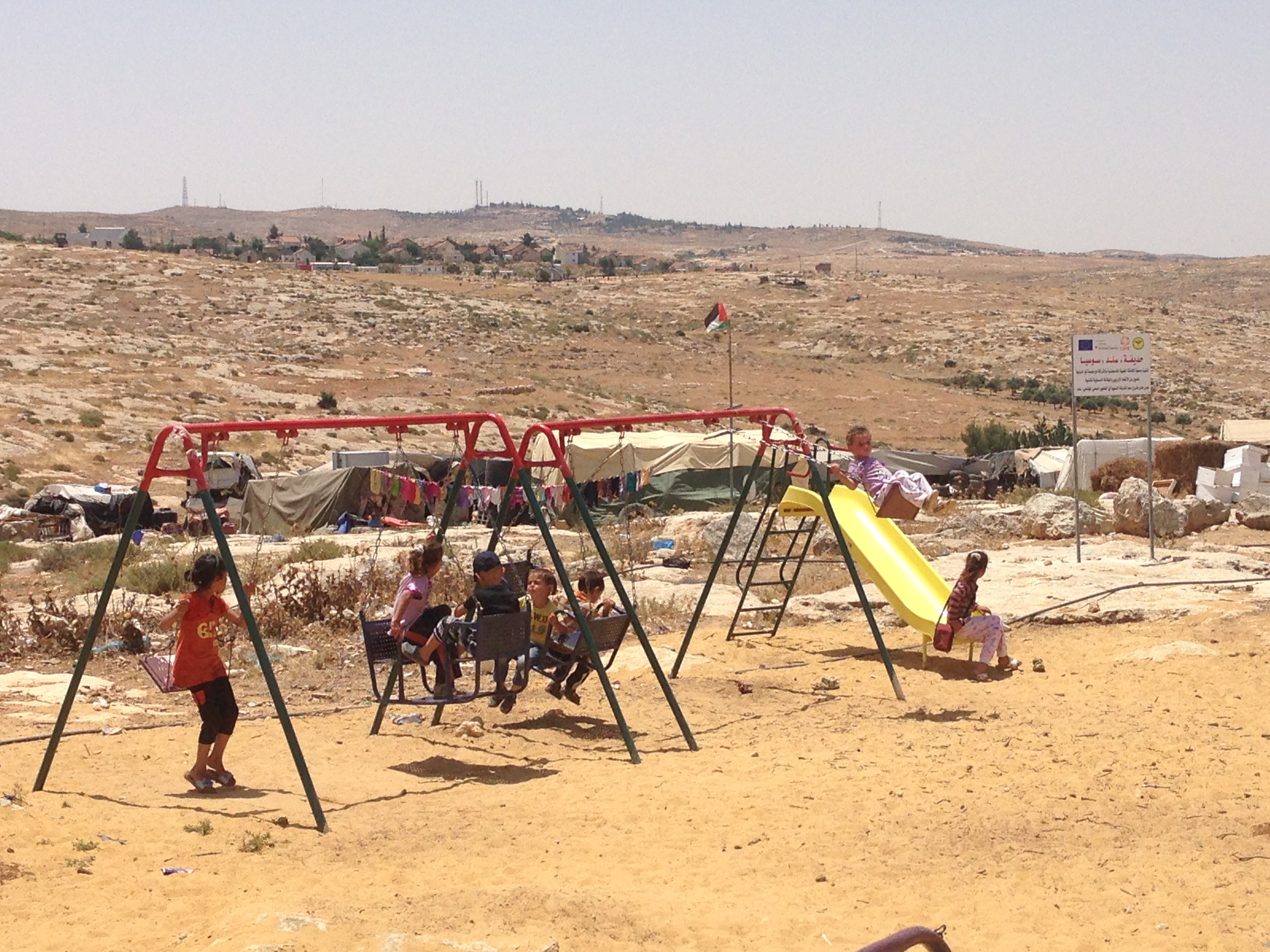 Children play at a playground in Susya - the Israeli settlement by the same name can be seen in the background. 