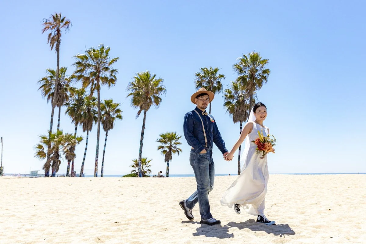 ベニスビーチの前撮りでヤシの木を背景にゆっくり歩く日本人夫婦の写真