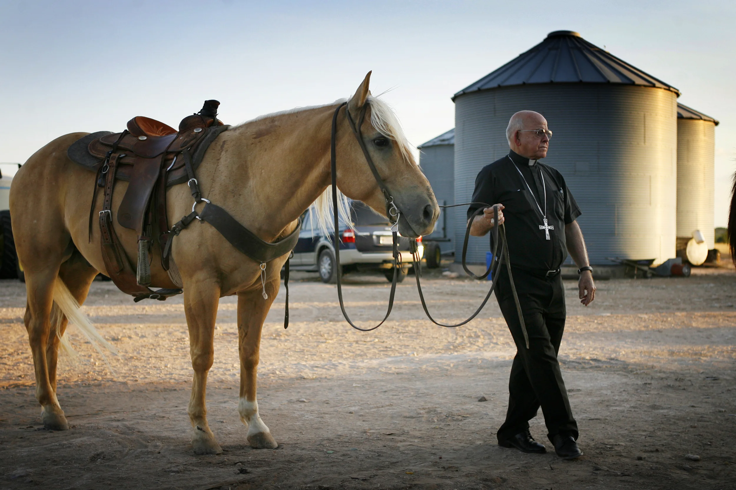  After leading a Rural Life Mass on the farm of Gary and Dinell Jacob near Winters, Bishop Michael Pfeifer, OMI, blesses horses brought to the mass. About 150 people from across the area attended the mass held in the shade of trees. 