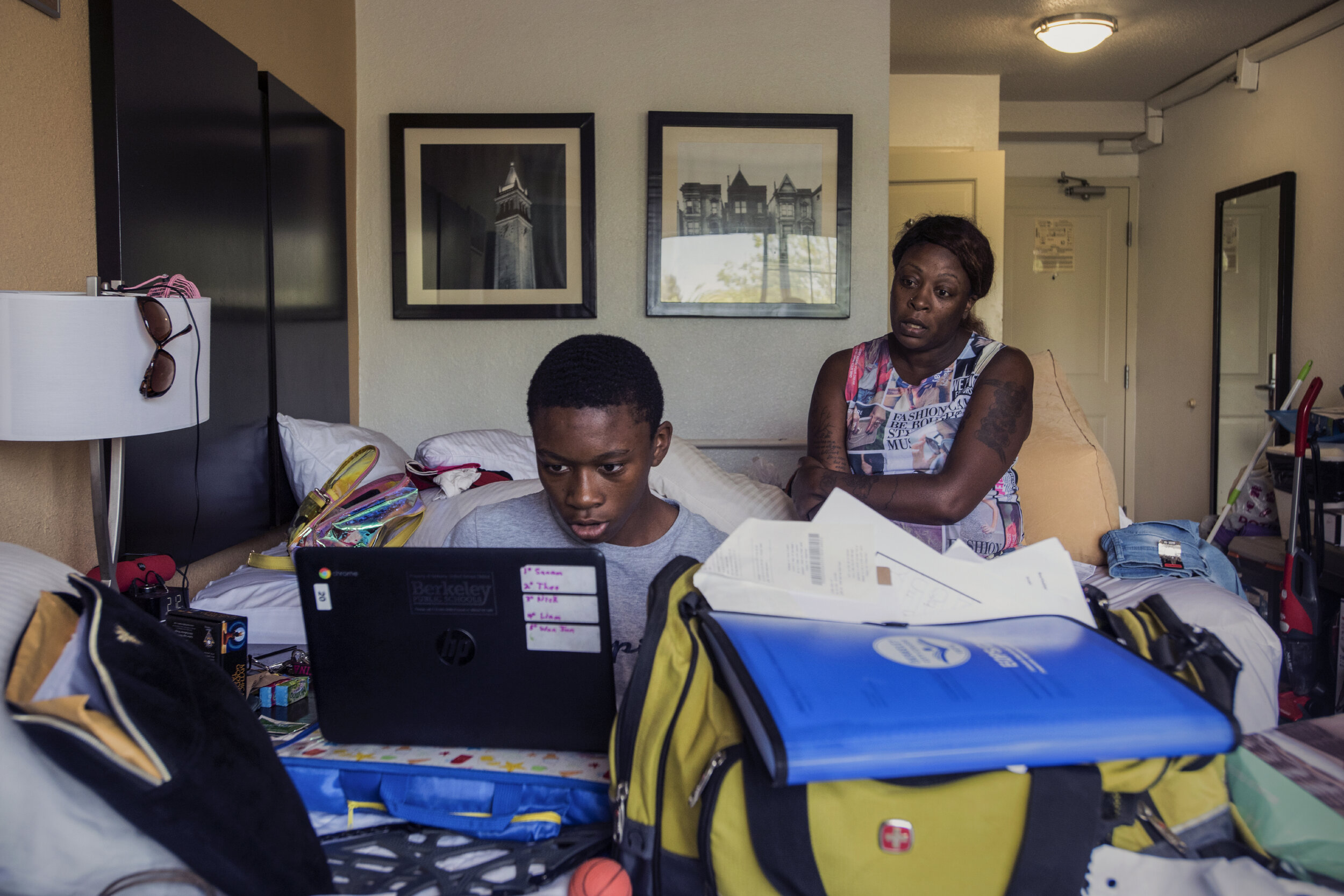  T watches her son K doing online classwork on his Chromebook in their Berkeley motel room. They just received notice that the school district has run out of money to subsidize their lodging costs and they will have to move to a shelter in the next t