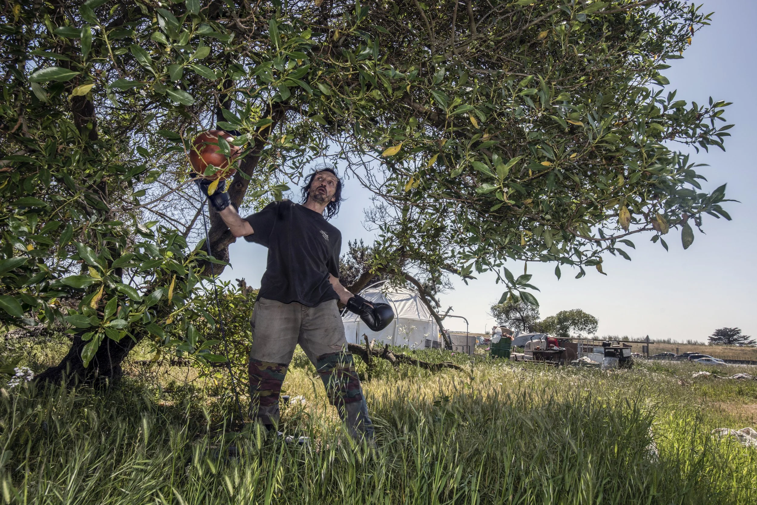  G works out hitting a punching bag that he has strung up near his tent on the freeway cloverleaf.  His camp has since been cleared by Caltrans. 