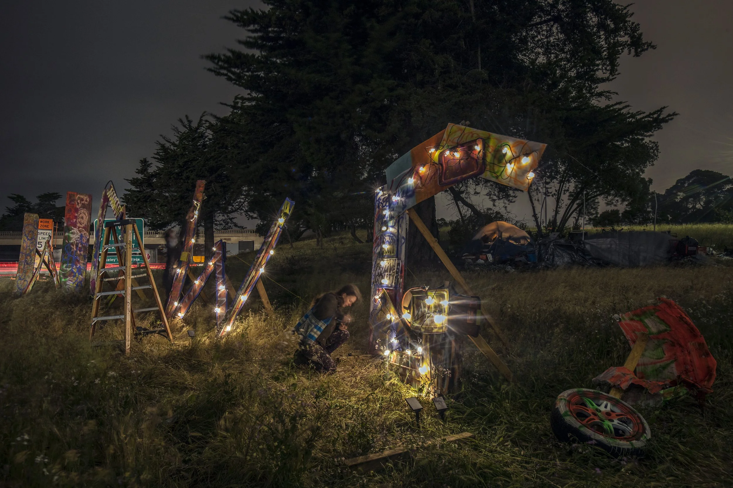  Berkeley, 2021.  Artist/activist Suzi Garner installs the letters WDWG (for Where Do We Go) by the Ashby/Shellmound freeway exit encampment, in support of the unhoused residents of Berkeley and Emeryville.  Caltrans took them down in less than a day