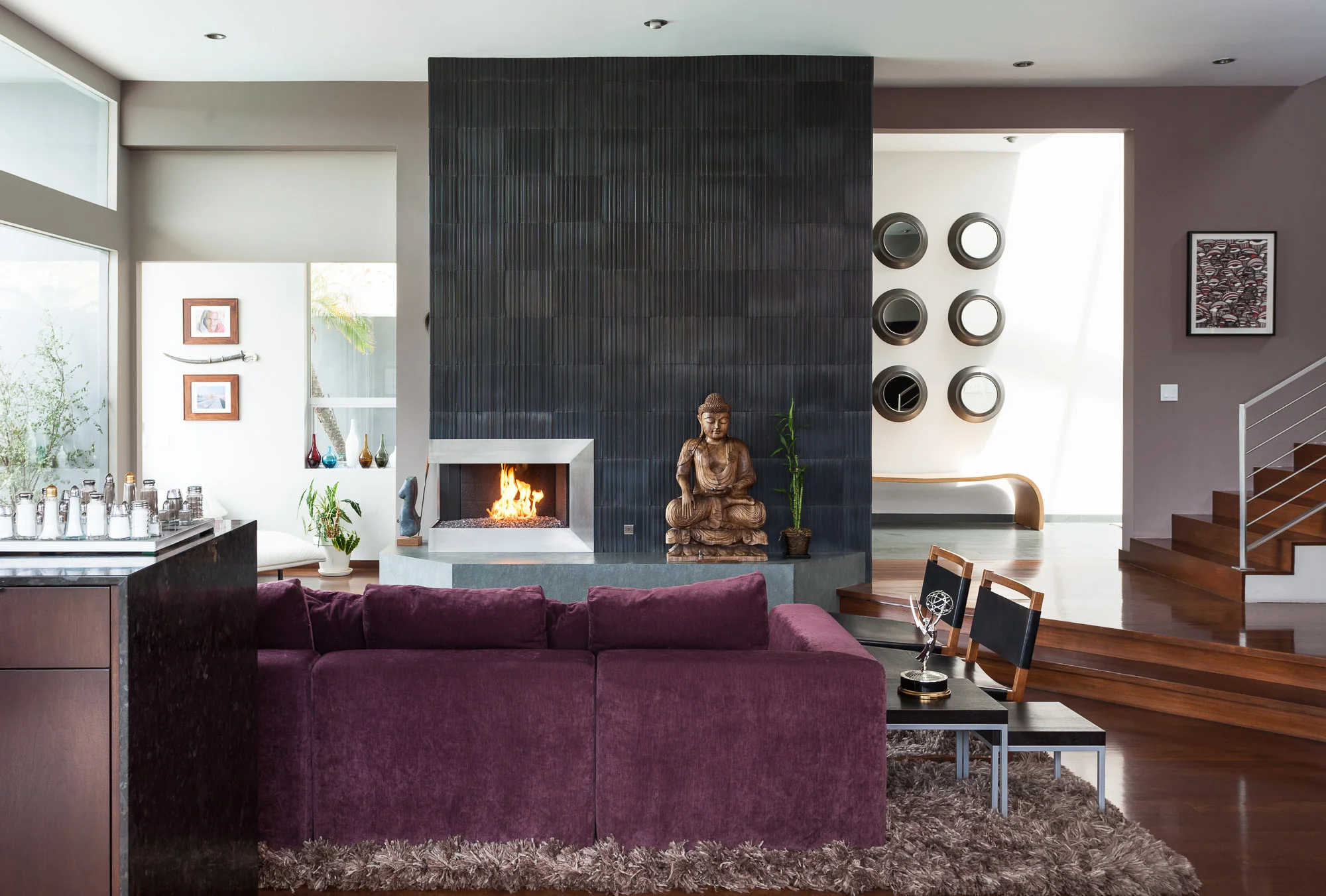 Celebrity-owned luxury home in Sherman Oaks, California featuring a modern living room with a purple sectional sofa, a fireplace, and a Buddha statue.
