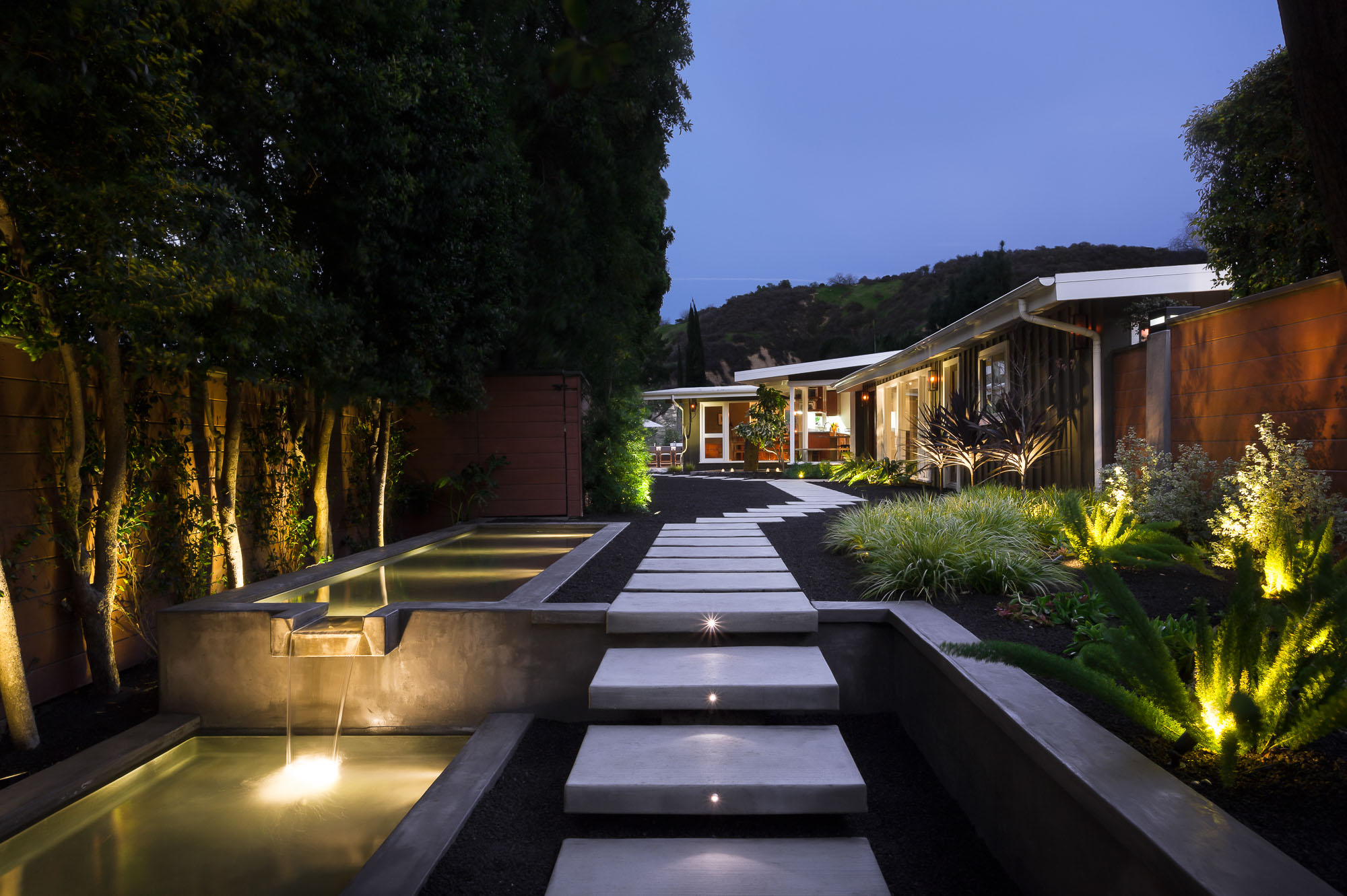 Mid-Century Modern home in Sherman Oaks with illuminated pathway, water features, and lush landscaping at dusk.