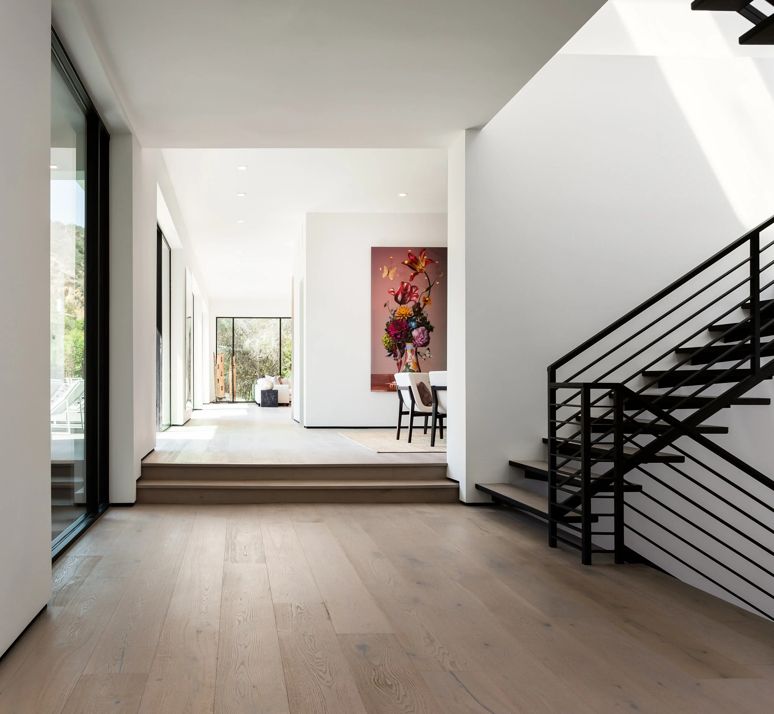 Modern interior of a luxury home in Beverly Hills, California, featuring sleek black staircase, light wood flooring, and large windows with natural light.