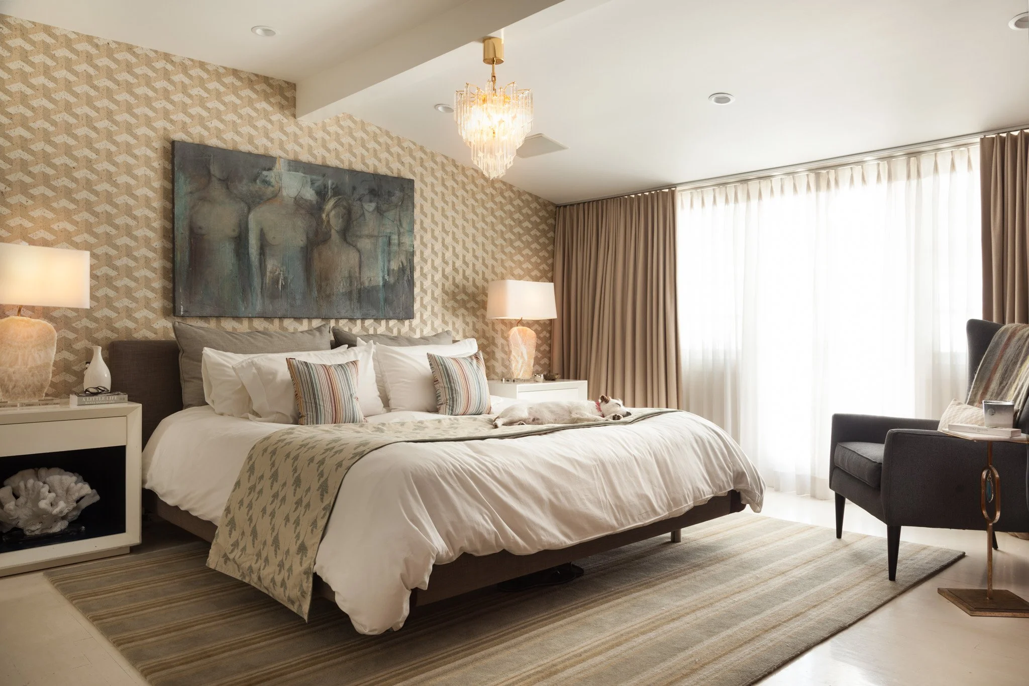 Luxurious bedroom in Nichols Canyon, Hollywood, California featuring a king-sized bed with patterned bedding, modern art, elegant chandelier, and natural light from large windows with sheer curtains.