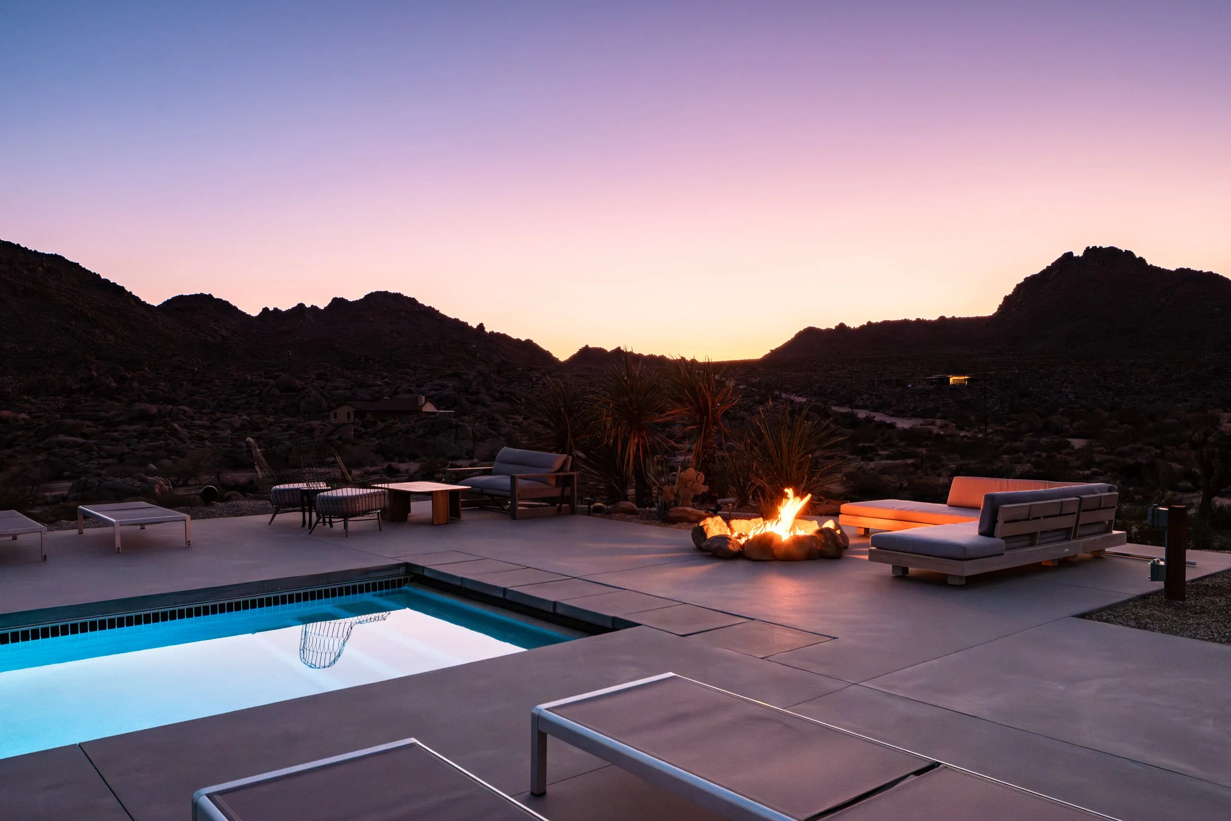 Sunrise at the Joshua Tree Country Club in Joshua Tree, California, featuring a serene poolside view with a fire pit and lounge chairs against a backdrop of desert mountains.