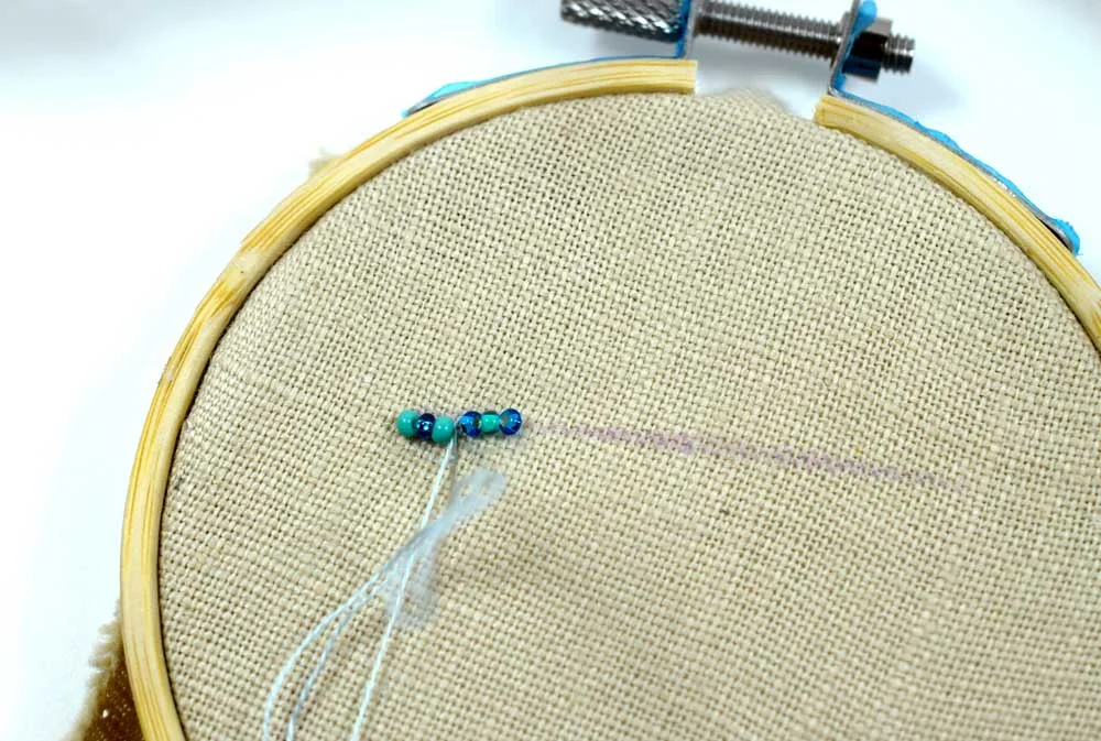 Bringing the needle back down into the fabric after running it through the first three beads.