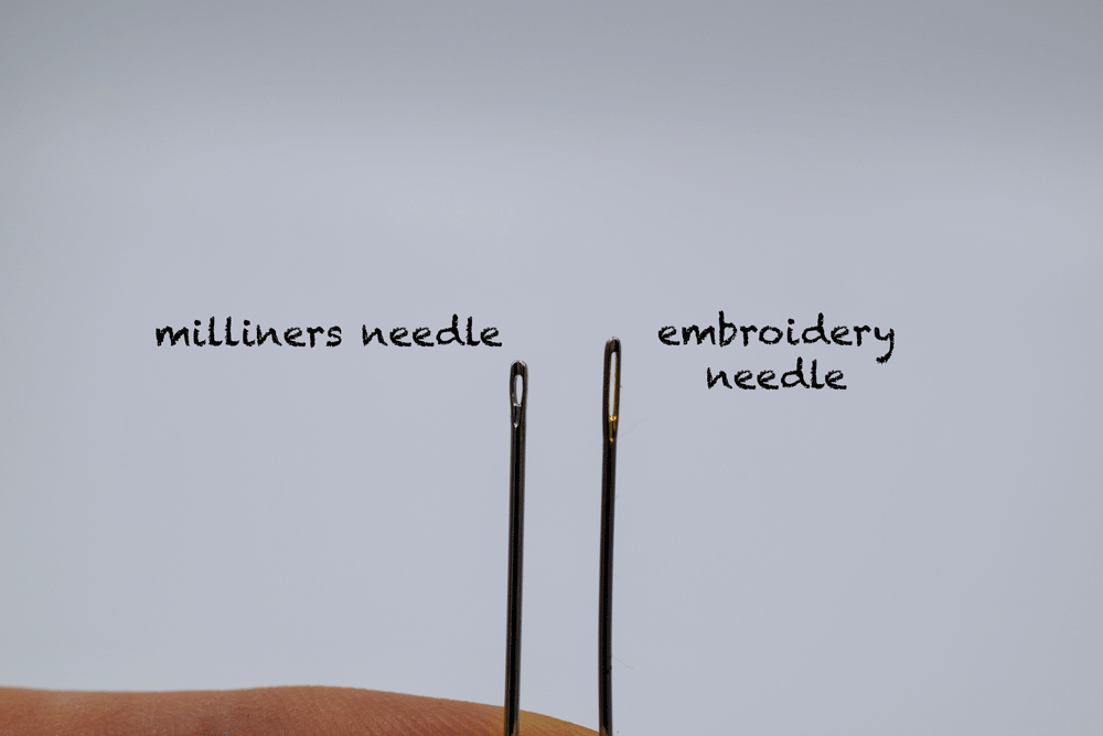 Above you see a milliners needle on the left and an embroidery needle on the right. What you can't see pictured is that the milliners needle is longer. See how the eye of the embroidery needle is a lot bigger and protrudes more?