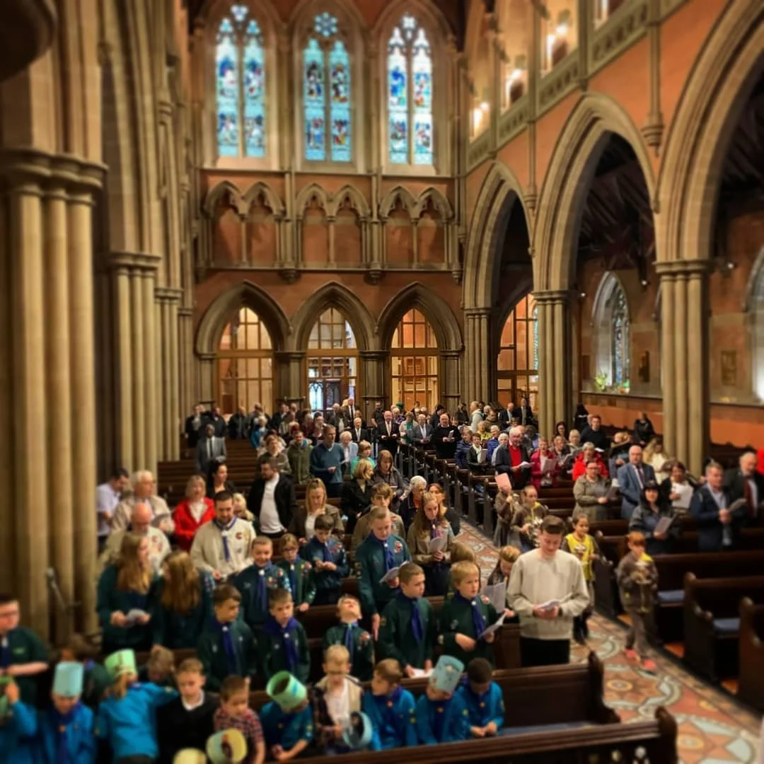 A large congregation gathered inside a Gothic-style church with stained glass windows and ornate architecture, participating in a service or ceremony.