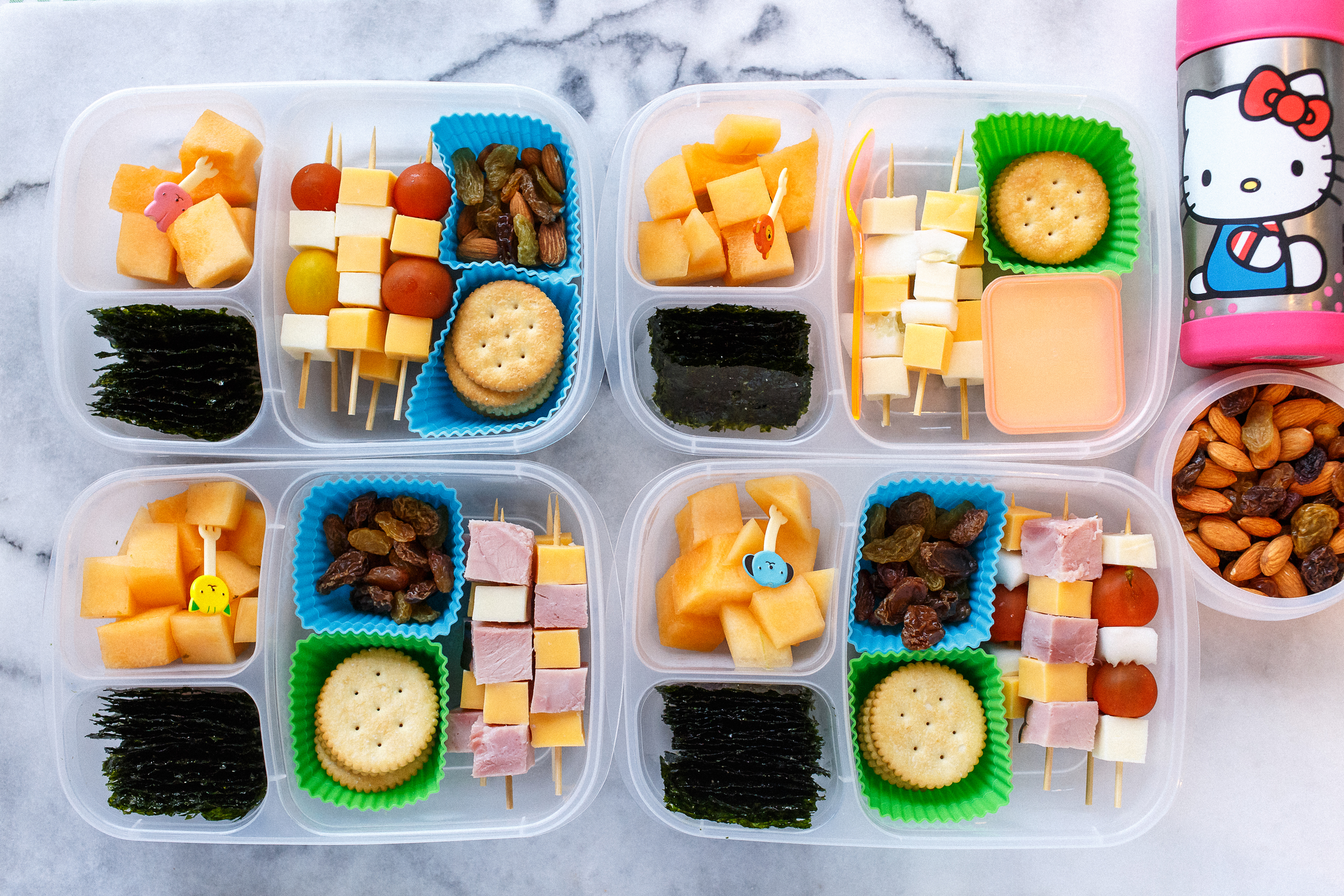 Little lunch skewers with a variety of ham, cheeses, tomatoes, and cucumbers, depending on who likes what. With raisins, seaweed snacks and melon. And the little one now has an extra side of nuts & raisins, and a thermos cup of milk.