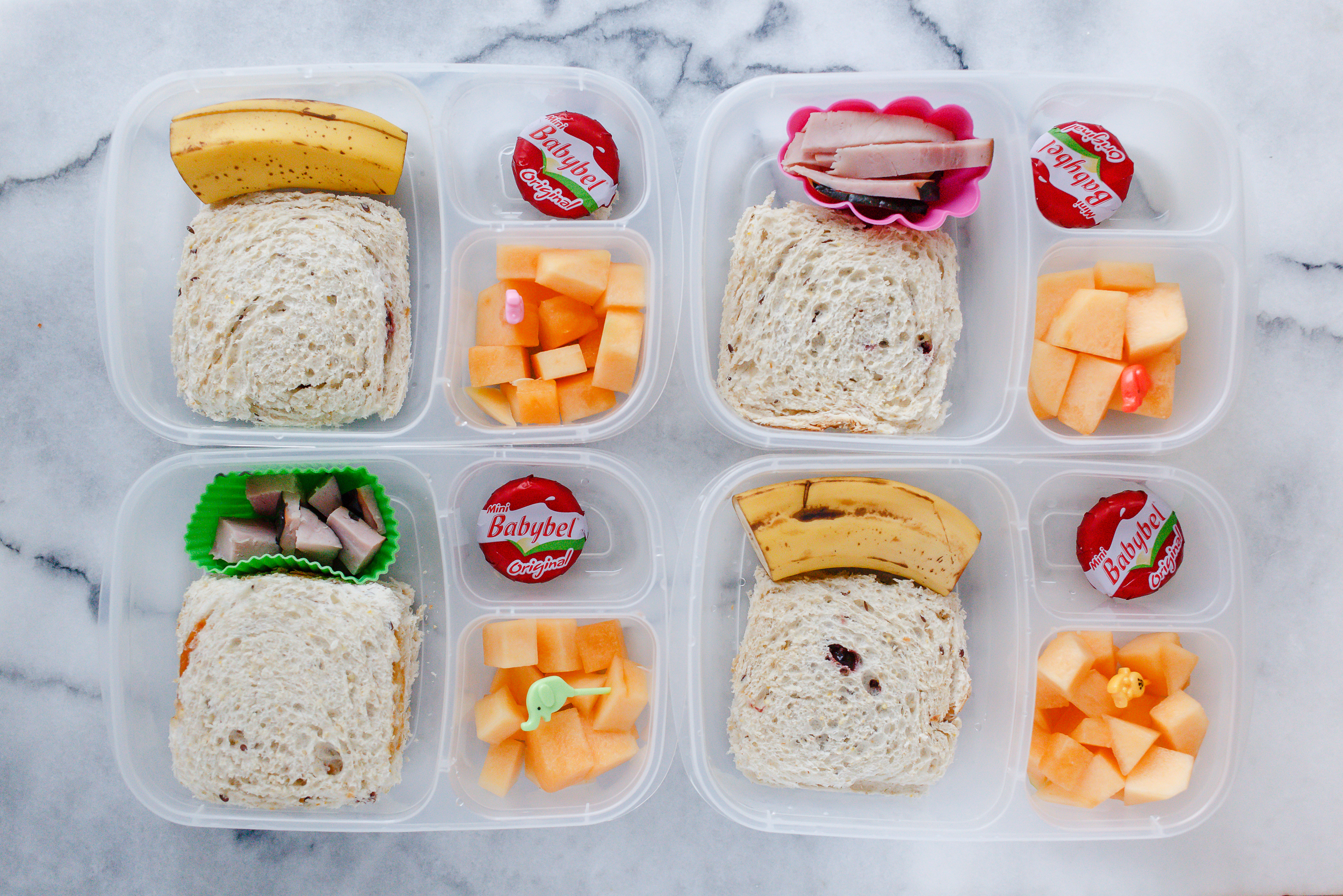 Little 'uncrustable' sandwiches, on 9 grain bread with homemade sunbutter and homemade jam, with melon and cheese. Two have ham, and two have banana. 