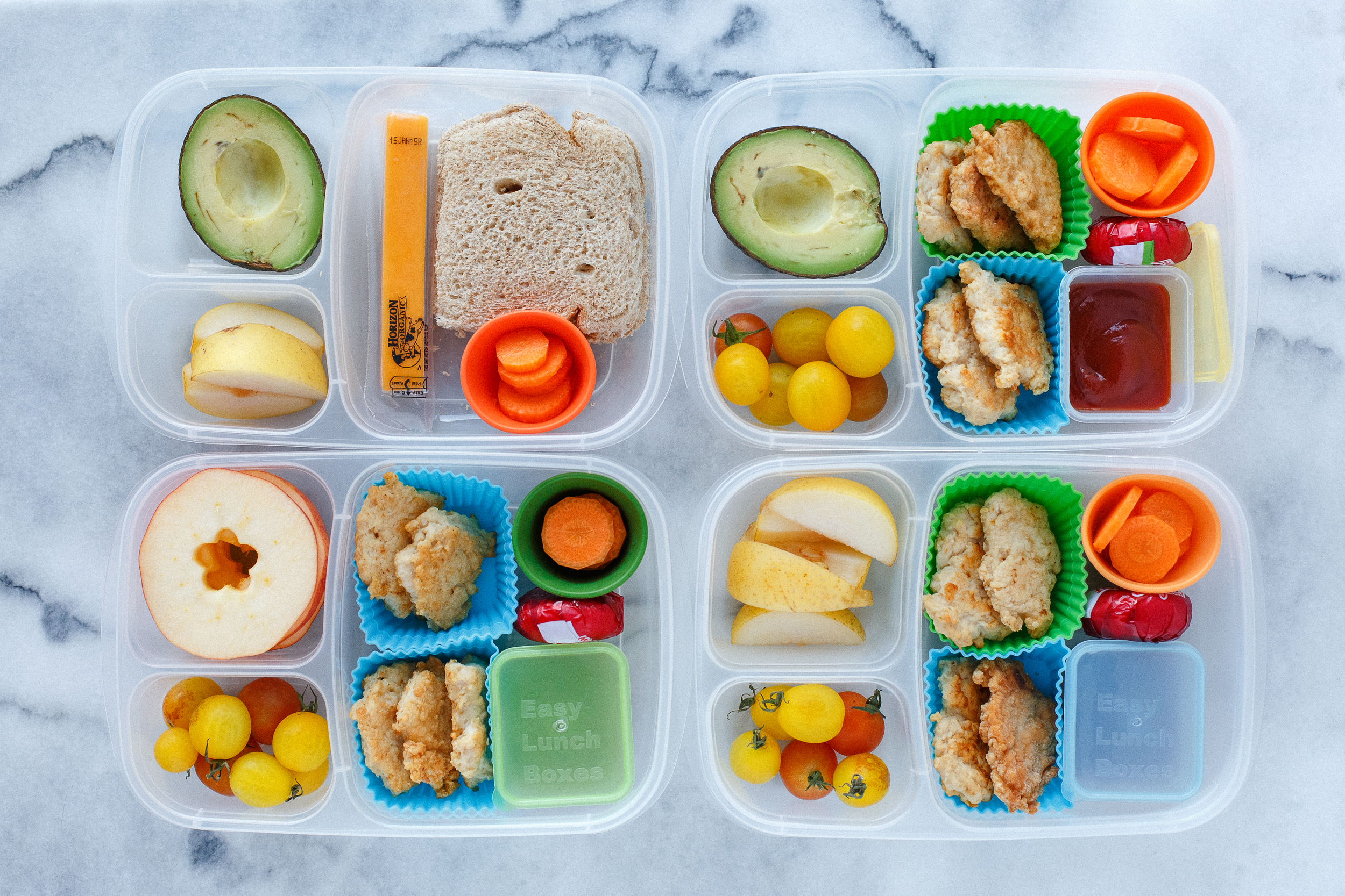 Three have leftover homemade chicken nuggets, with ketchup for dipping. One doesn't eat meat so she has sunbutter and jam sandwich. With cheeses, carrots, pears, tomatoes, and an avocado half for two. 