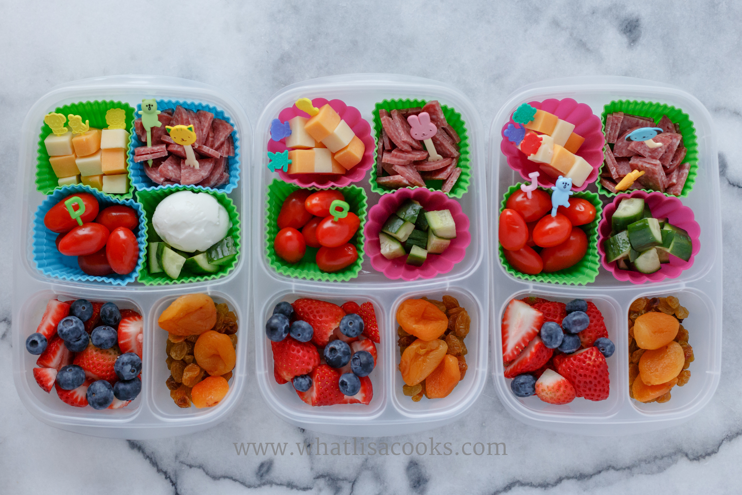 Grain free lunch. Cubes of cheddar and jack cheese, salami, tomatoes, cucumbers, strawberries, blueberries, raisins, apricots, and one has a boiled egg. 