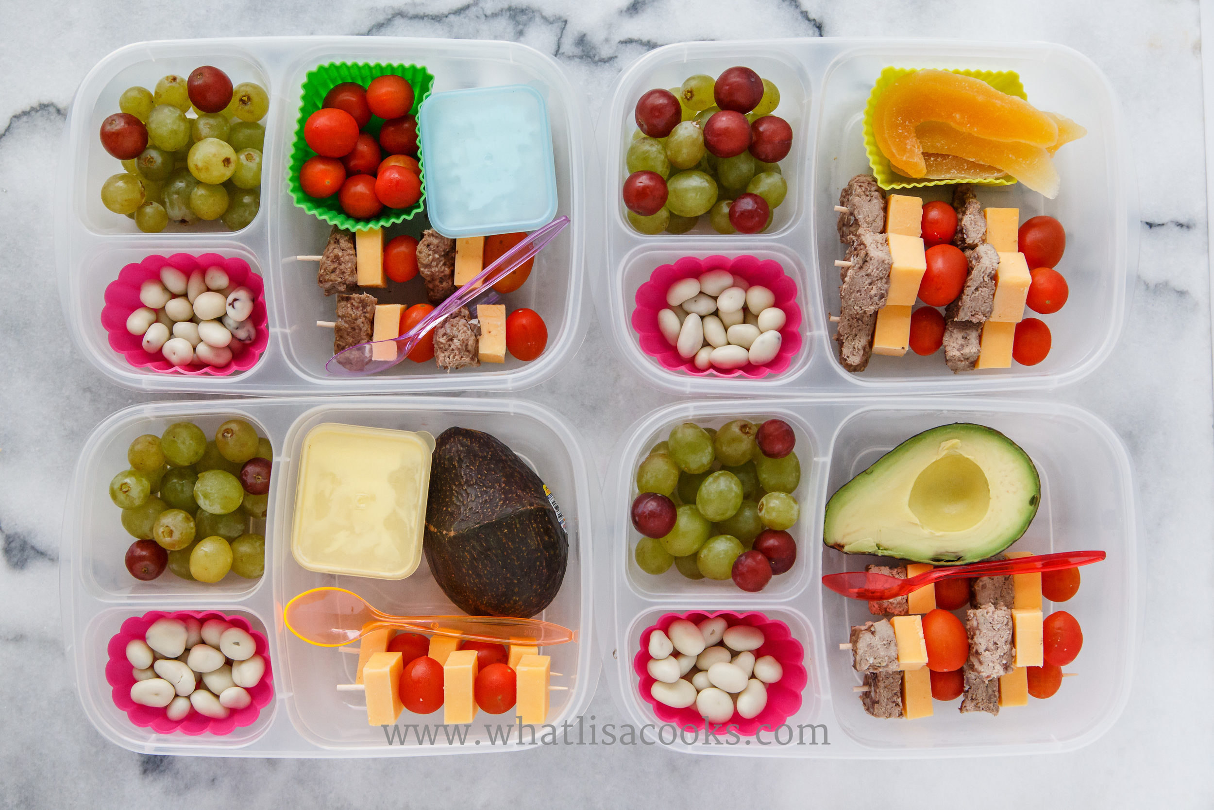 Bunless burger sticks: bites of homemade hamburger patty, cheese, tomatoes on skewers. Grapes and yogurt covered raisins on the side. Two have avocado, one has dried mango, one has yogurt, one has cottage cheese. 