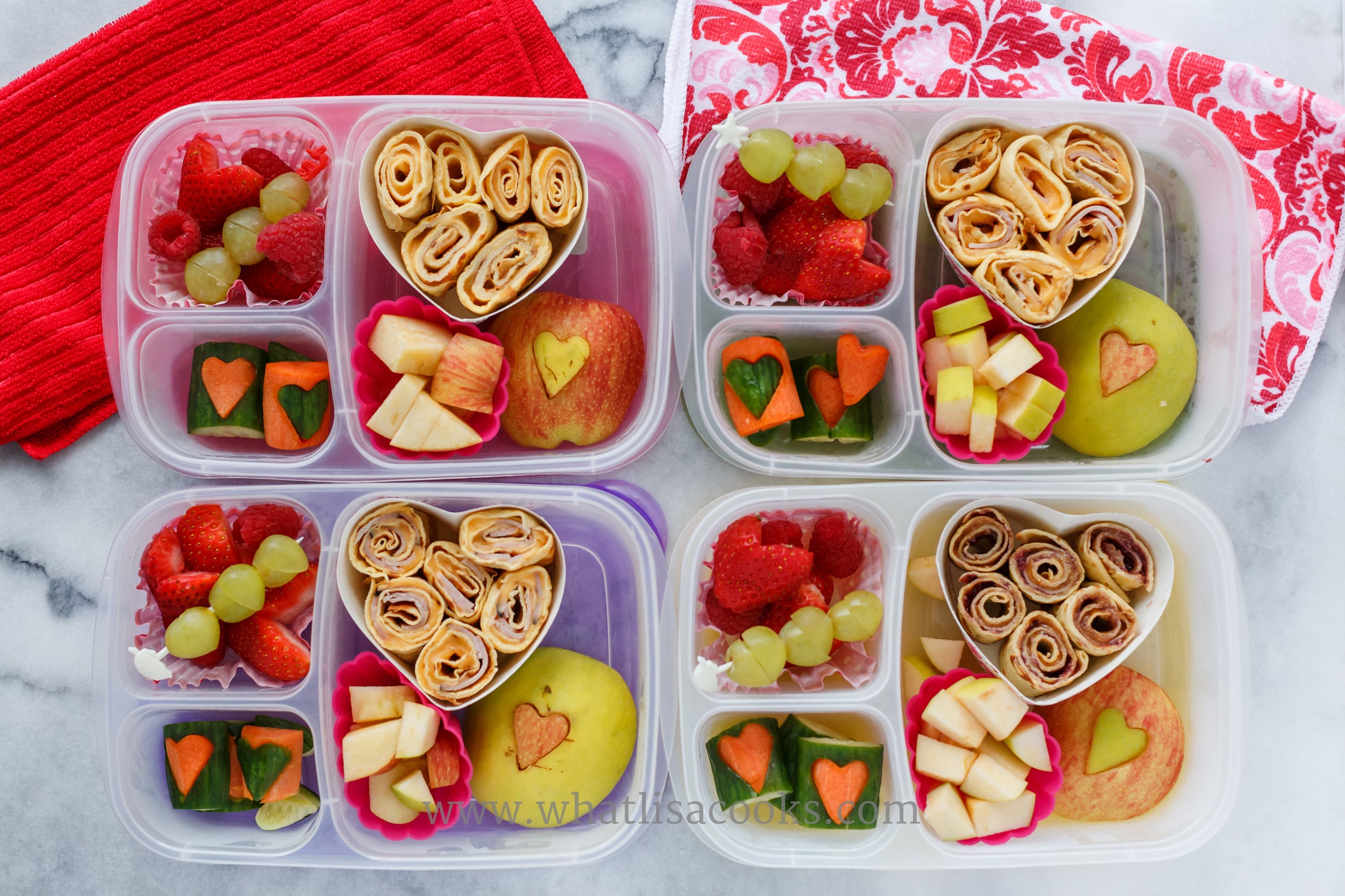 Crepe rolls with cheese and ham, apples with heart cutouts, carrots and cucumbers with heart cutouts, grapes and strawberries. 
