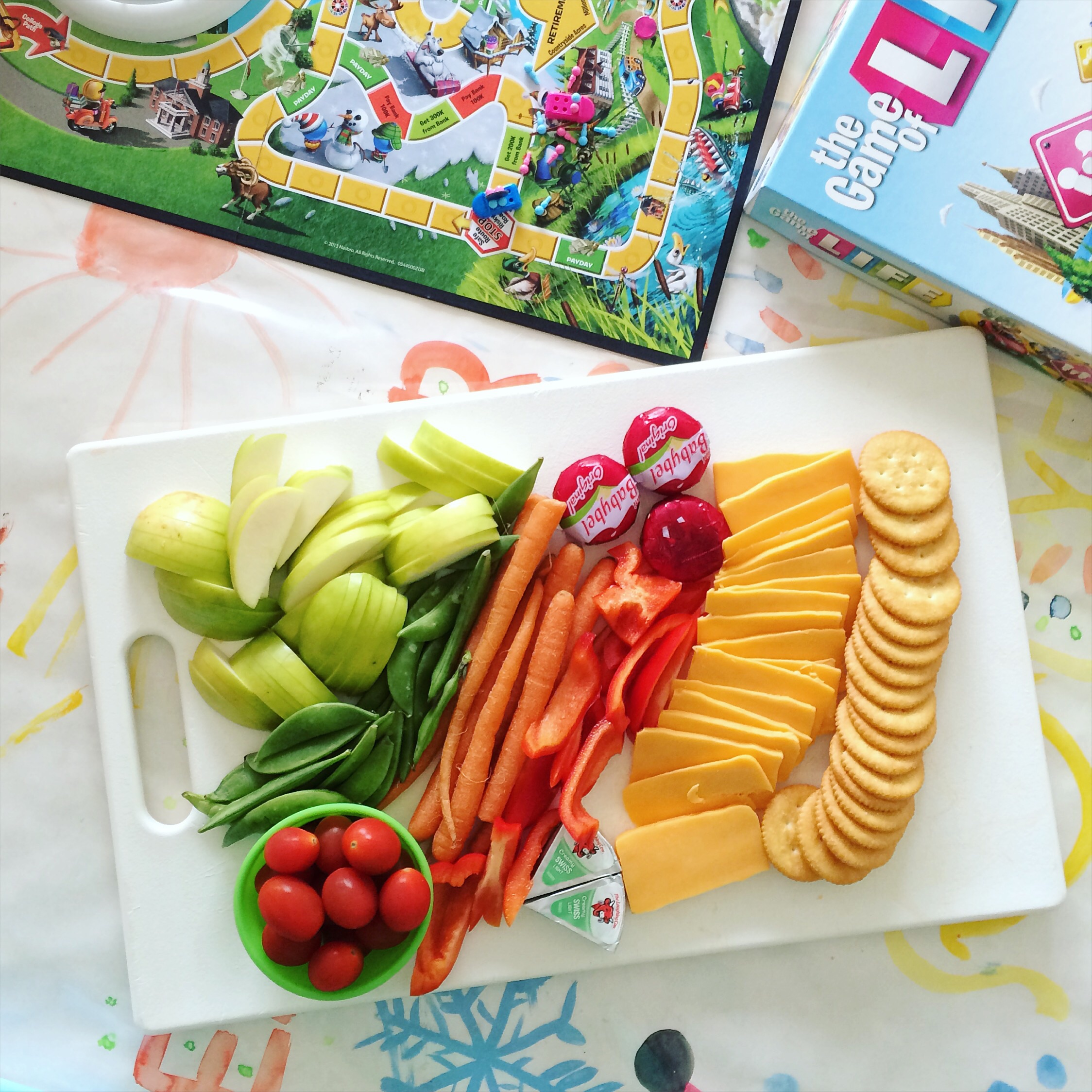a cutting board with cut up fruit, vegetables, crackers, and cheese