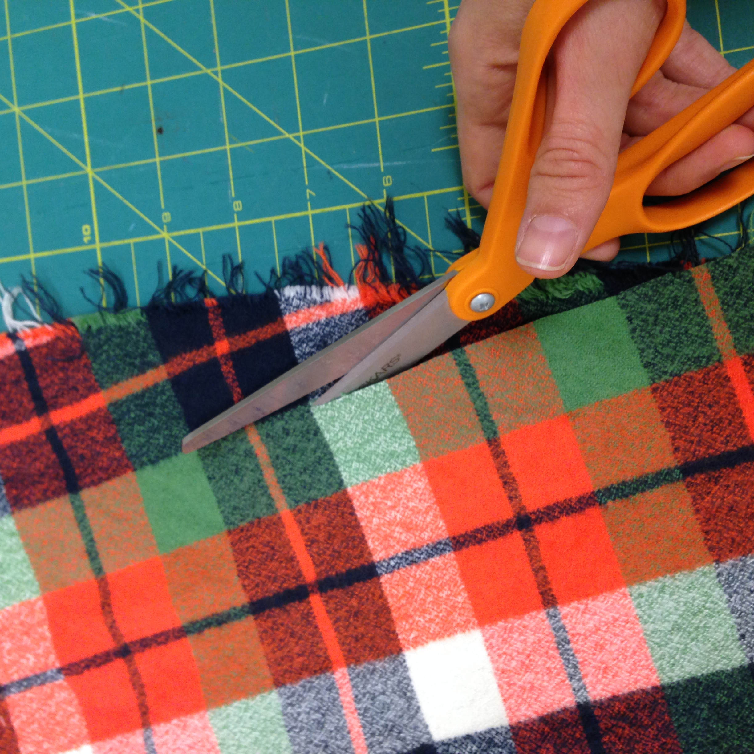 Cutting along the edge of the green stripe of the fabric to find the grain.