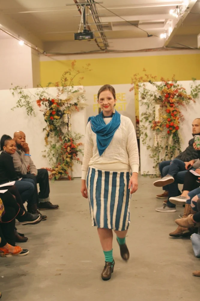 Jillian wears an indigo terry skirt with reverse terry stripes made from scraps and a shirt made from an antique linen tablecloth. Underneath she wears a mock neck tee from Vivant Vintage. Her indigo velvet scarf is by Dyer Maker and her earrings are by Peston.