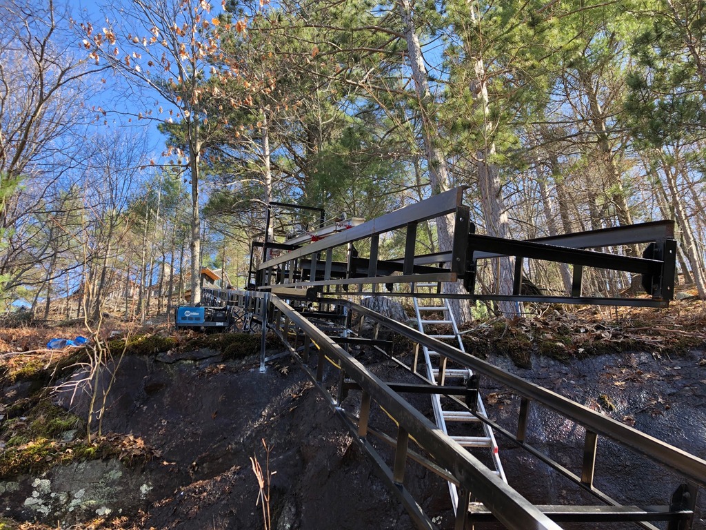 Looking up the track at the finished top curve and 200’ on to the cottage. The installation hoist is carrying a 20’ section of track to the third pitch. This change in angle is small in degrees but pretty obvious at 20’.