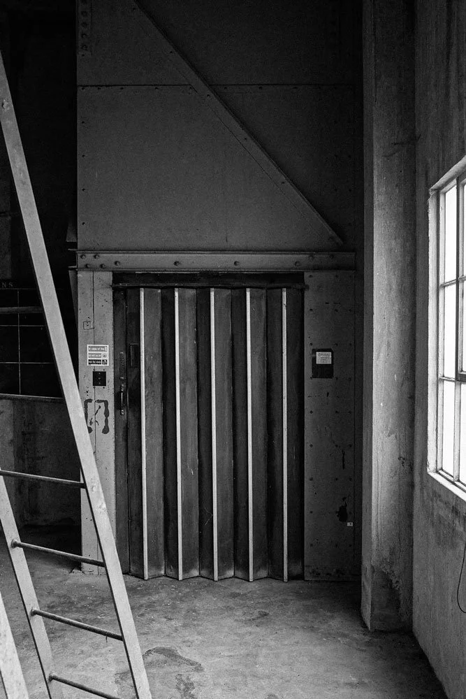 An industrial elevator with wood paneling on the doors, next to a window in a concrete room.