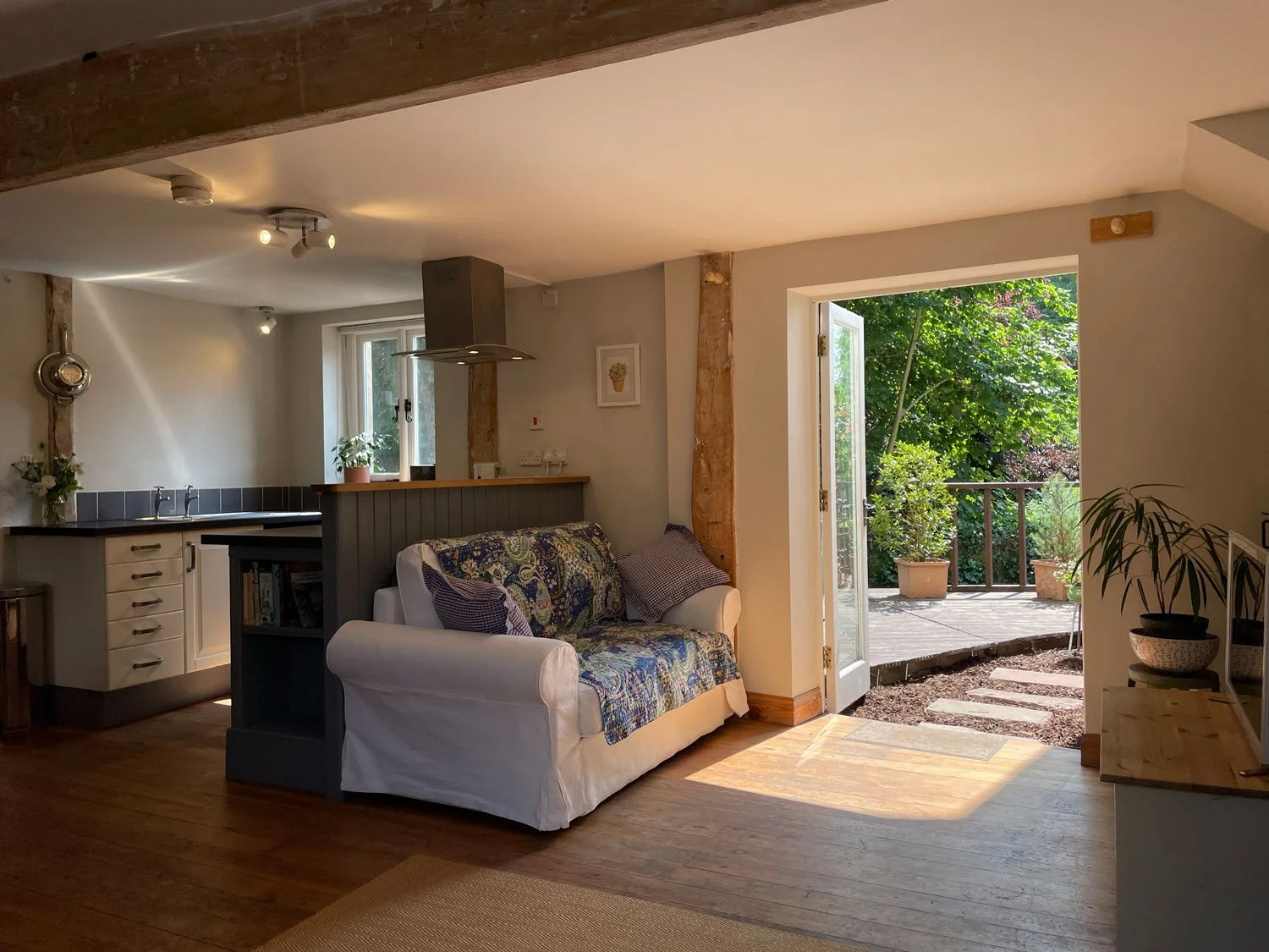 Living room with an open door leading to a patio with potted plants and trees outside.