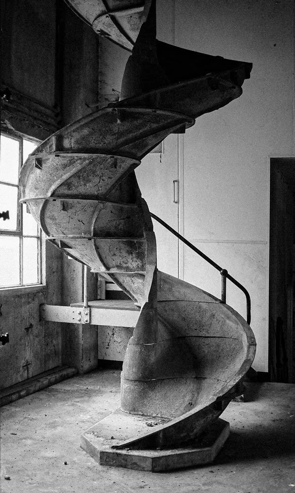 Black and white photo of an old, weathered spiral staircase inside a building.