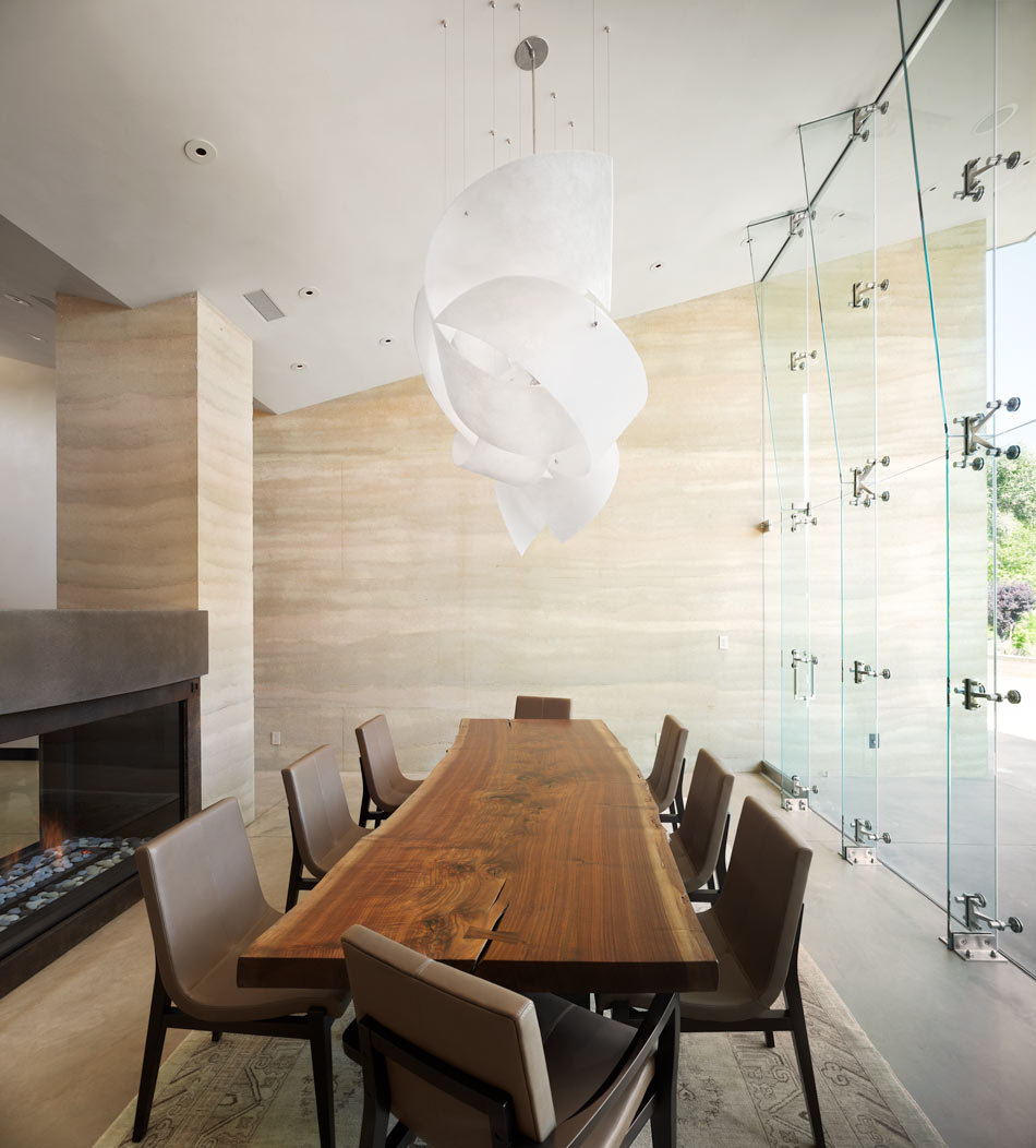 Continuing the color weave, fifteen foot high shed walls define the dining room which opens to the south. More massive pilasters store heat from the gas fireplace. The glass wall dies into rabbets in the earth, bringing profuse light into the space and allowing the room to radiate with warmth. Image © Adrián Gregorutti