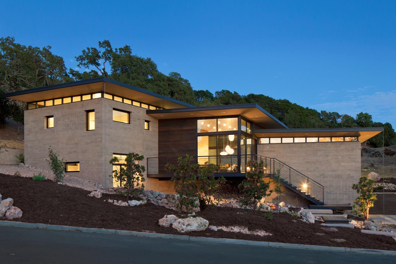 Backlit evening view displays surrounding clerestories and floating roofs. Here the relationship of the rammed earth block to its site is clear. A building site like this, where excavation is required, can provide more than enough soil to make the blocks. Image © Mark Luthringer