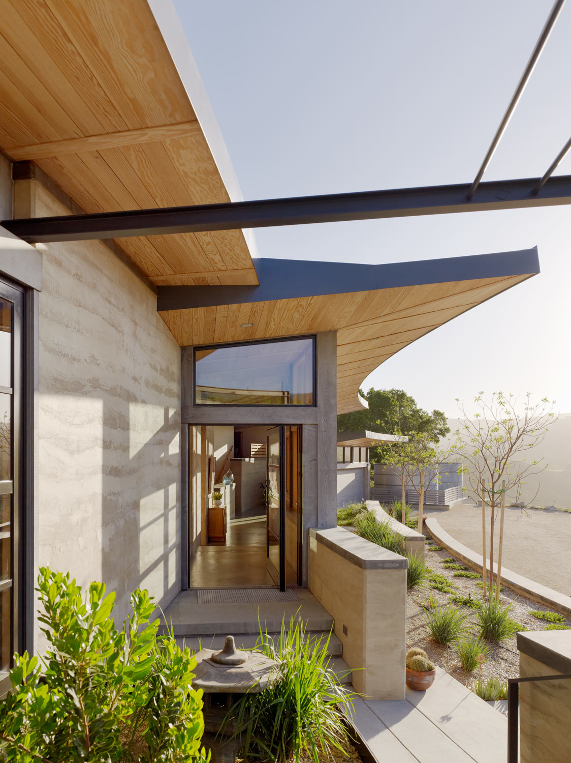 The shallow curves of the house walls repeat themselves in the low patio and planter walls. Capturing rainwater for irrigation, three tanks proudly sit close to the home - a clear sign of the available water resources for landscape. Image © Joe Fletcher